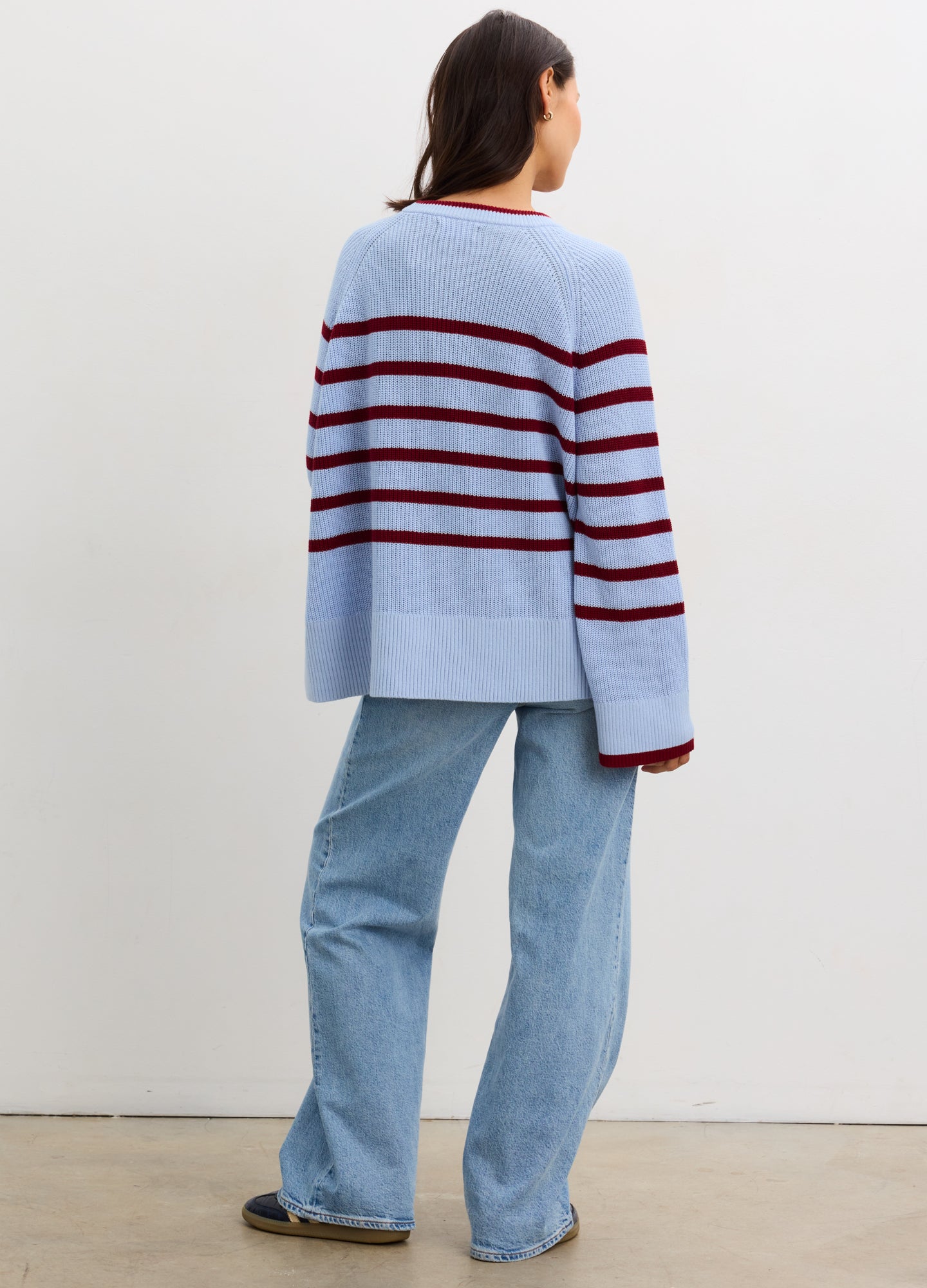 Pregnant woman wearing a blue and red striped sweater with jeans against a plain background