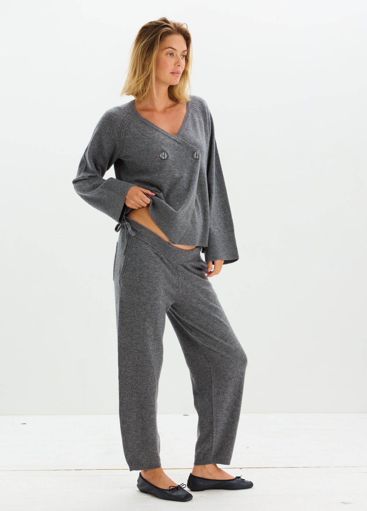 Woman wearing a charcoal gray cashmere lounge set with a wrap-style top and adjustable drawstring pants.