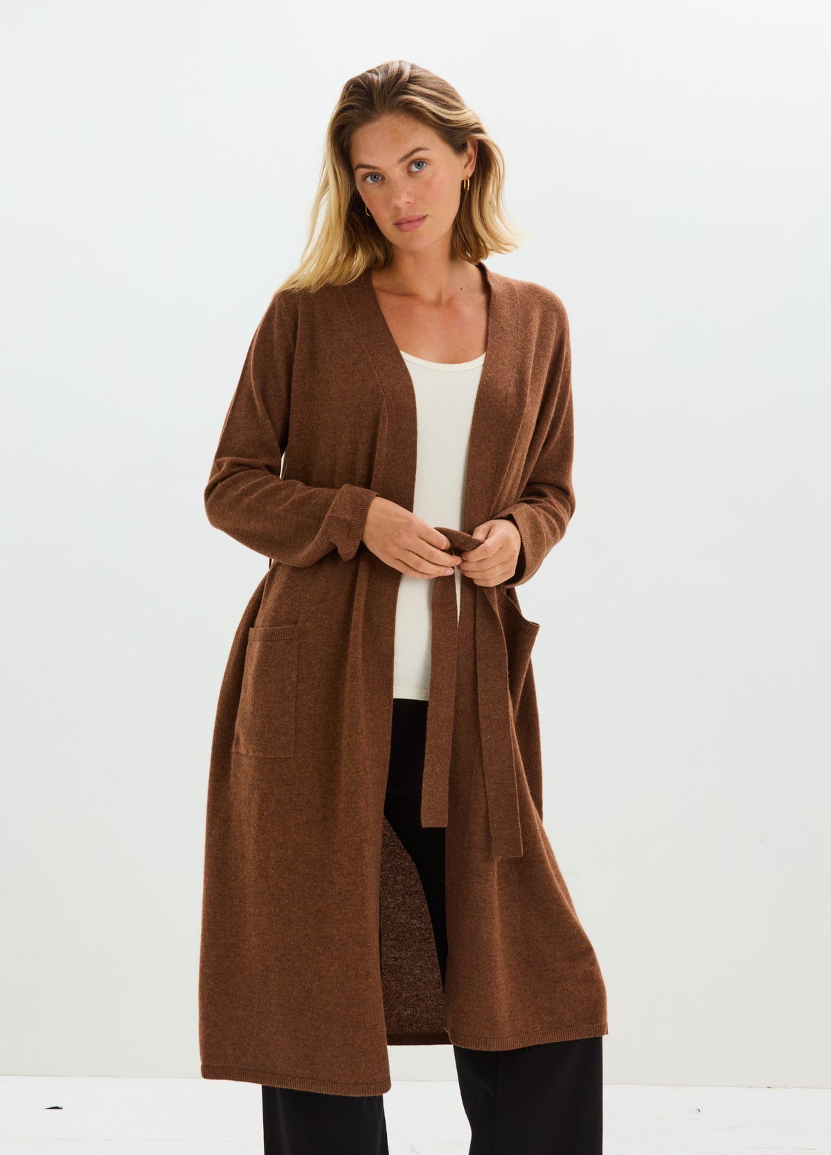 Woman wearing a long, open-front chocolate-brown cashmere robe with a matching waist tie and side pockets.