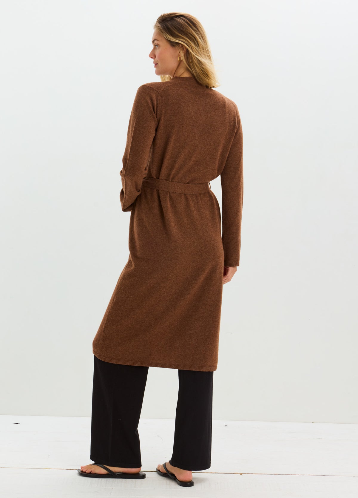 Woman wearing a long, rust-brown cashmere robe with a tied waist over black trousers.