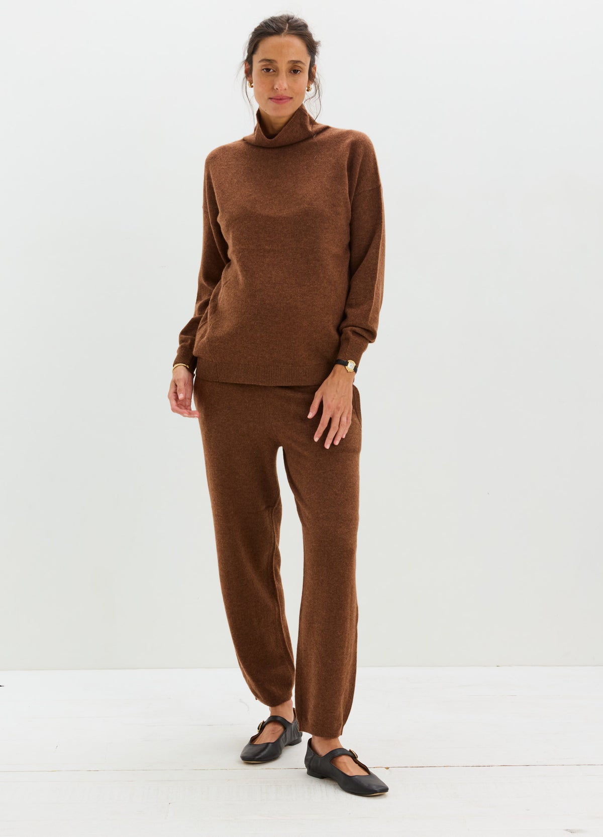 Model wearing a matching brown cashmere set with a relaxed turtleneck sweater and tapered pants.