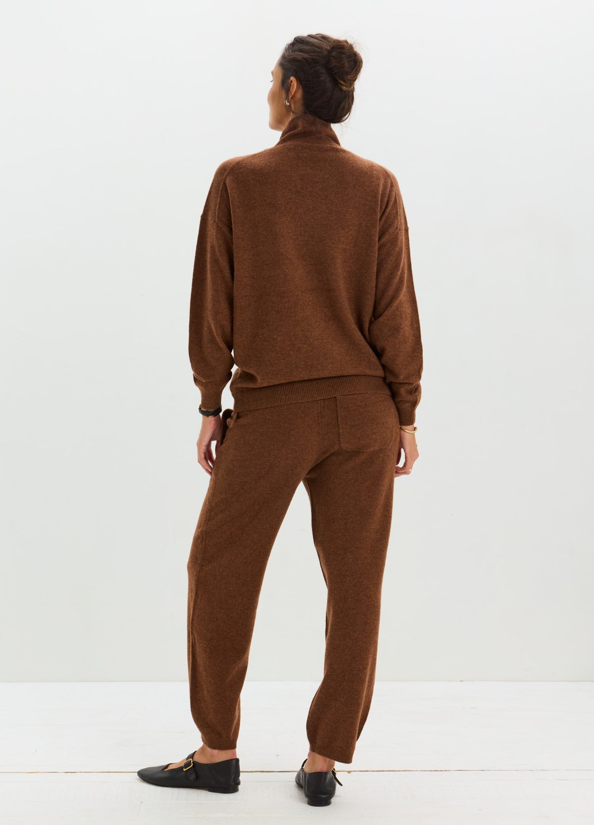 Woman wearing a matching brown cashmere sweater and trousers, with a relaxed fit and ribbed cuffs.