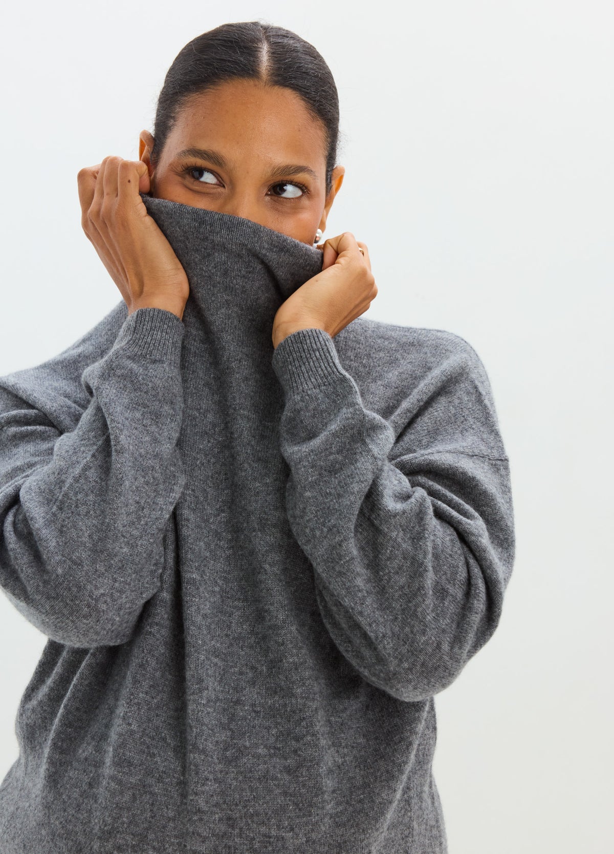 Charcoal gray cashmere sweater with a soft, oversized fit and high neckline pulled over the lower face.
