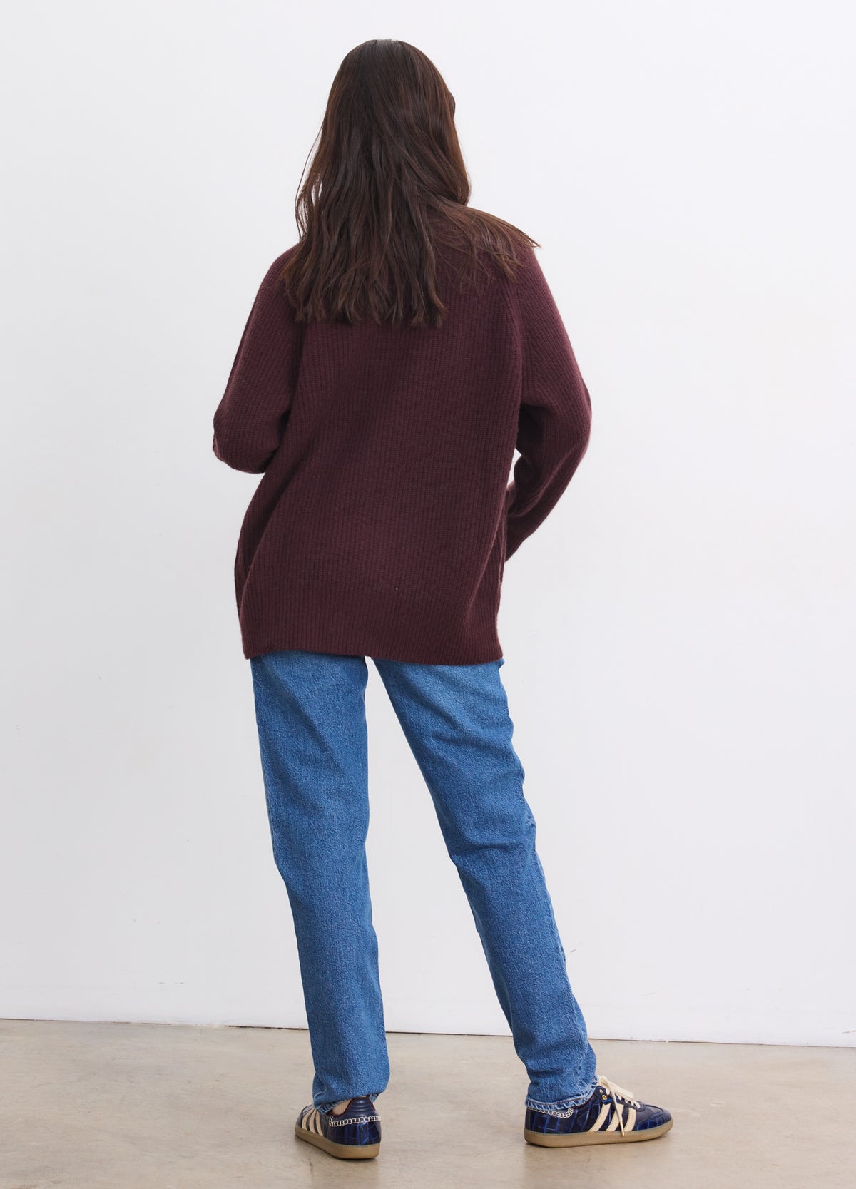 Long burgundy cashmere cardigan with a relaxed fit, worn over casual blue jeans and sneakers.
