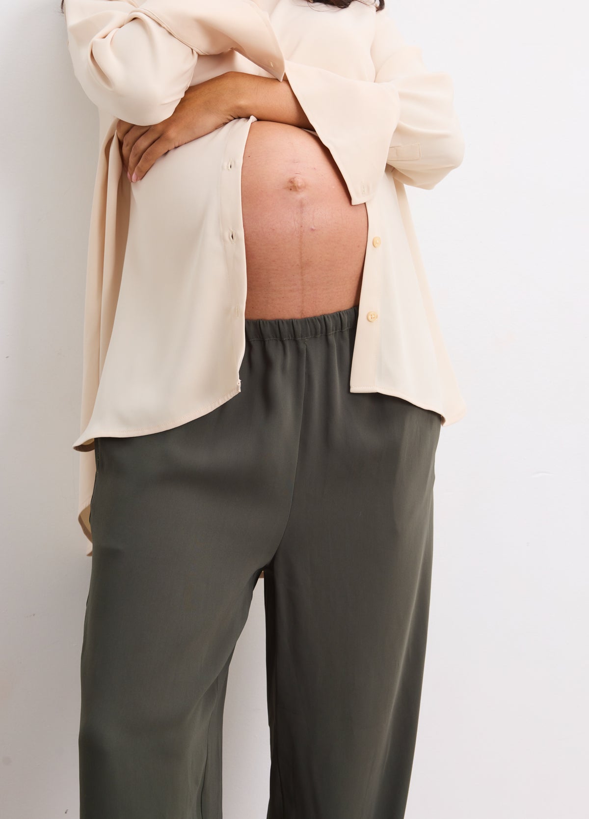 Maternity pull-on pants in basil green with elastic waistband, worn by pregnant model with beige shirt.