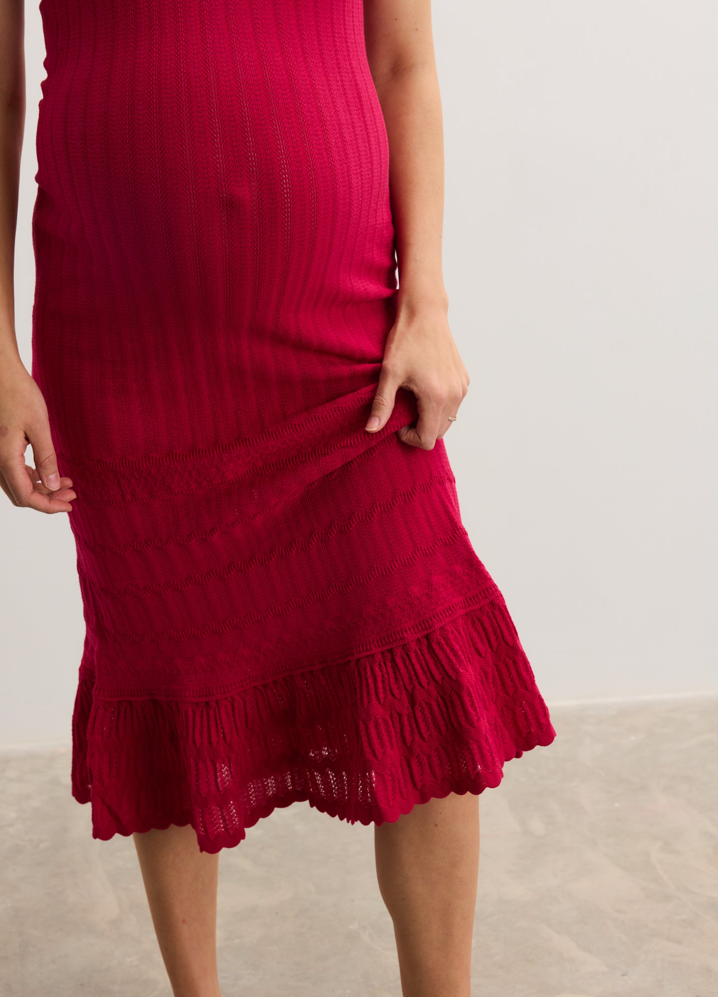 Bright red ribbed knit maternity dress with fitted silhouette and flounce hem, designed for pregnant comfort.