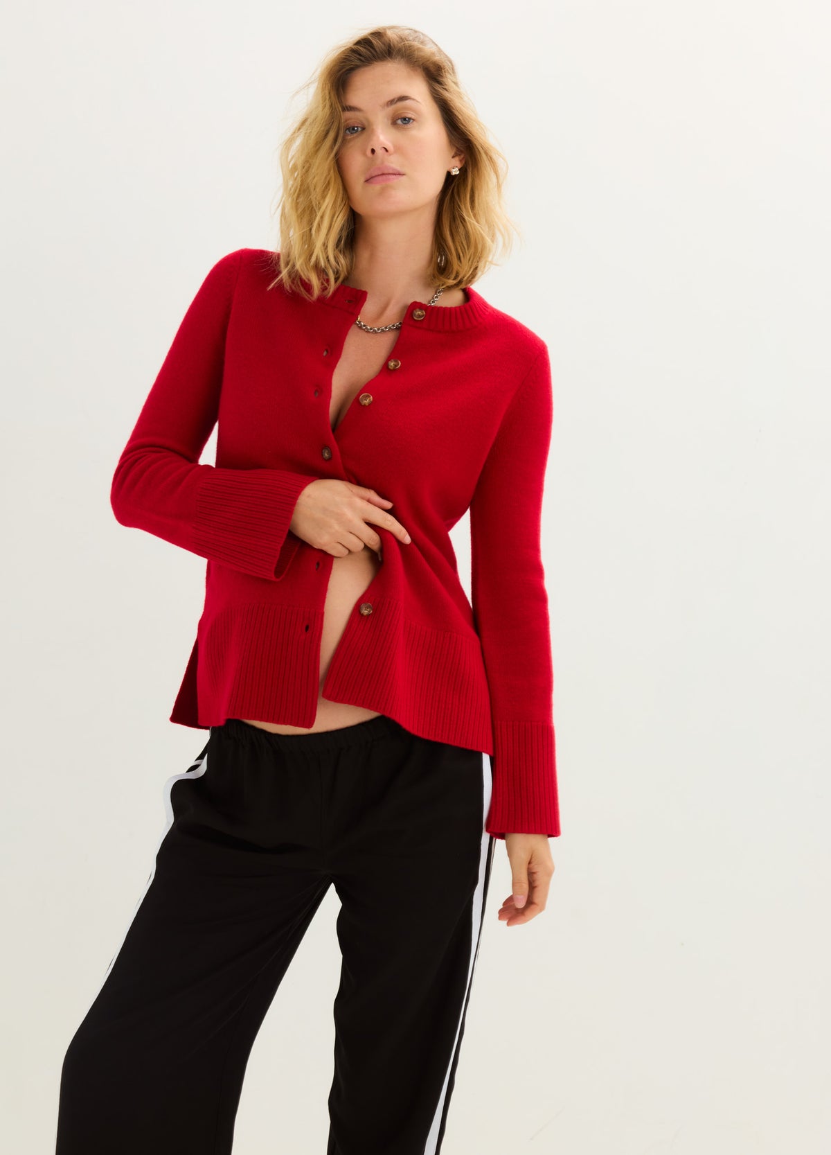Red fitted knit cardigan with button front and peplum hem, styled open over maternity wear.