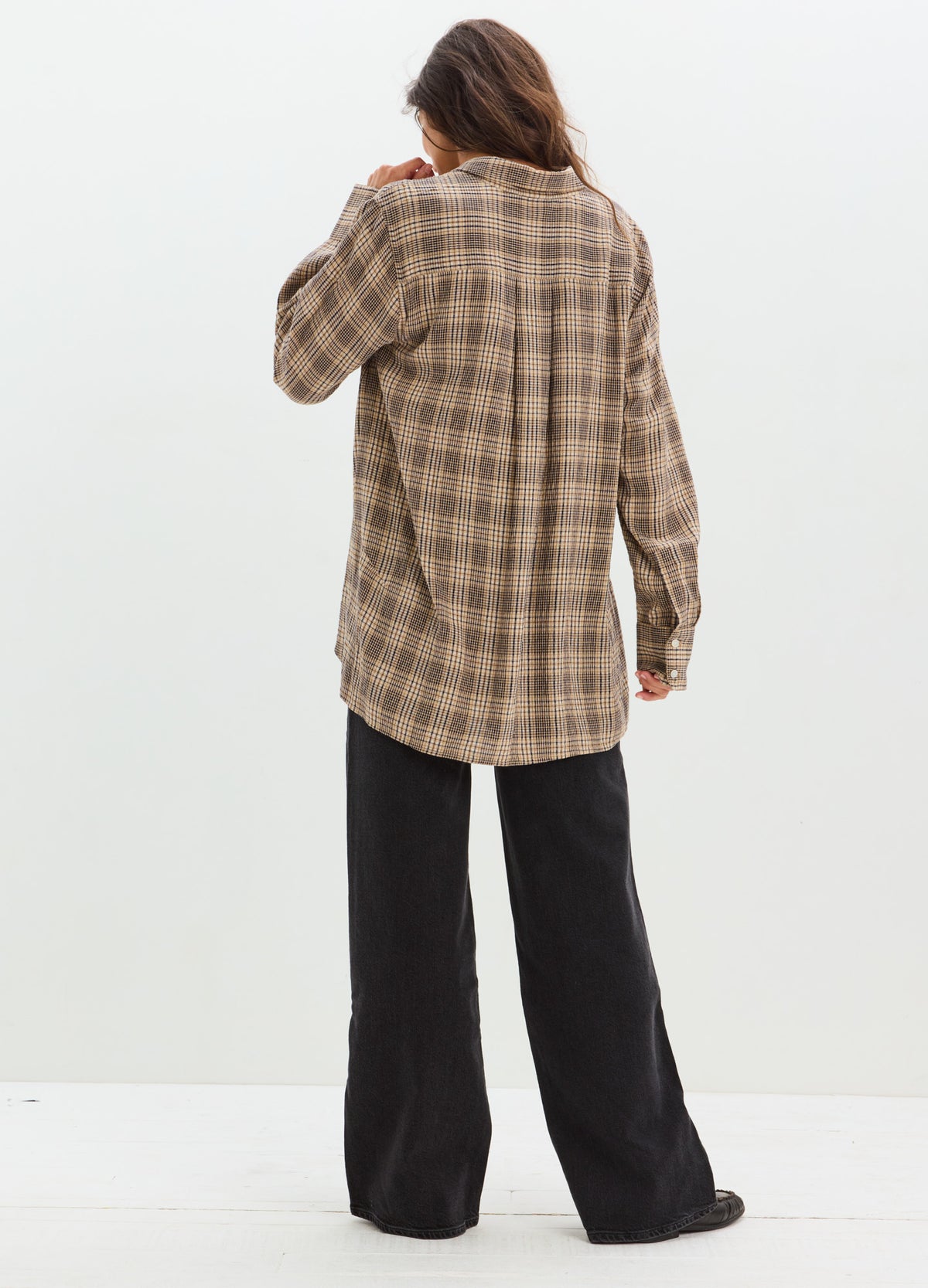 Brown and beige plaid maternity button-down shirt with long sleeves, worn loose over black wide-leg pants.