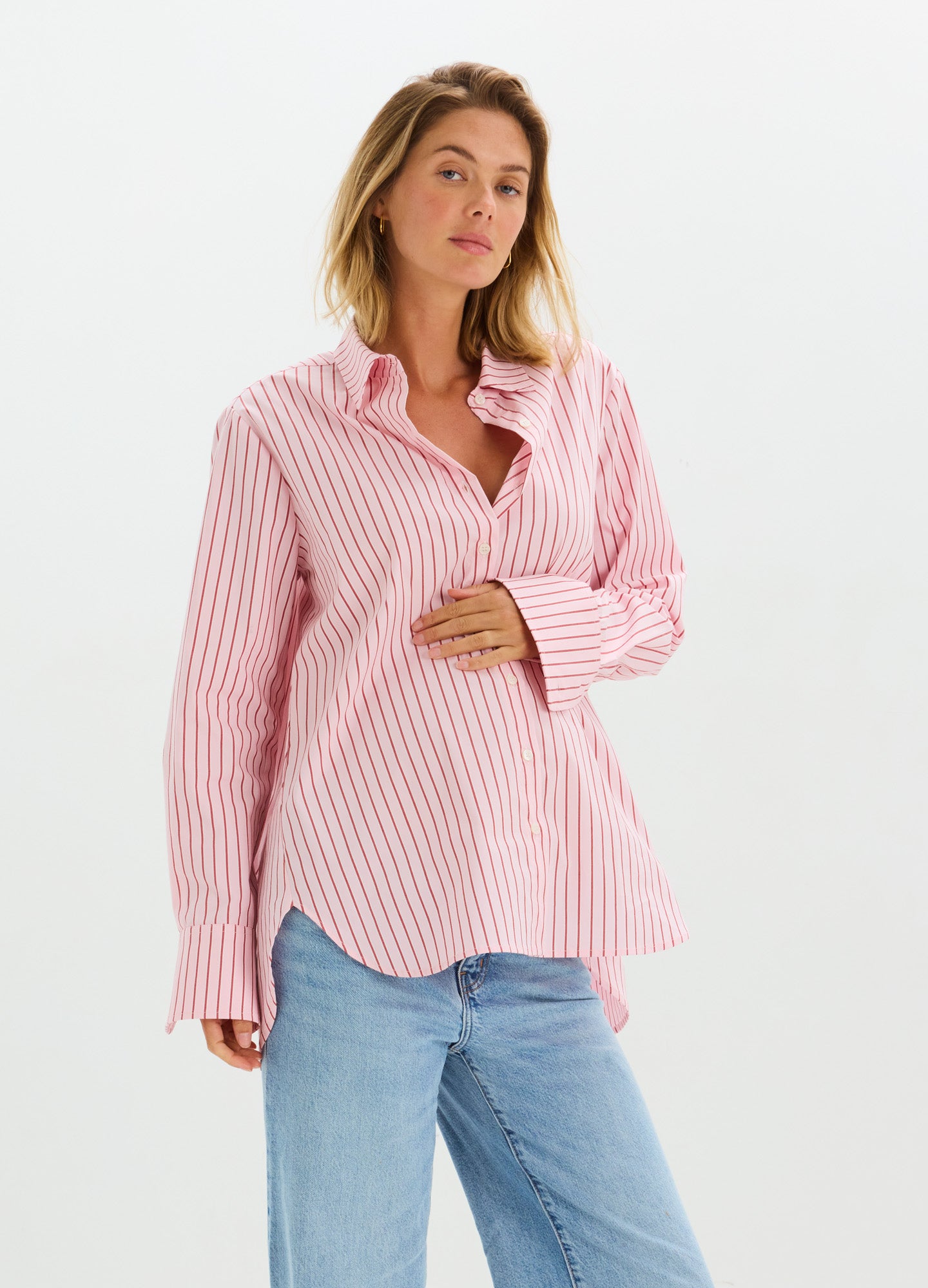 Pink and white striped long-sleeve maternity button-down shirt with relaxed fit, worn with blue jeans.