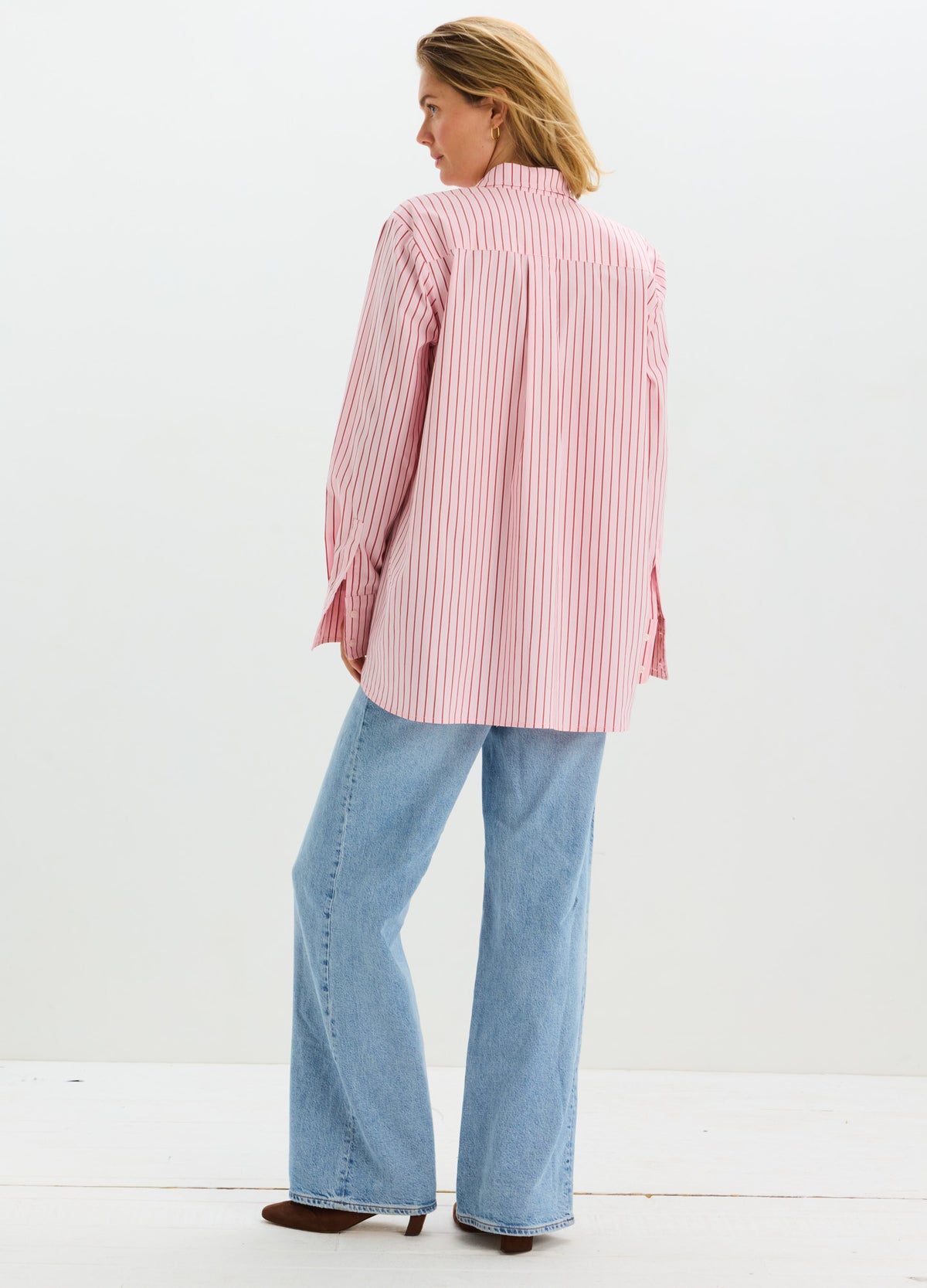 Pink and white striped long-sleeve maternity buttondown shirt with a relaxed fit, worn with light blue jeans.