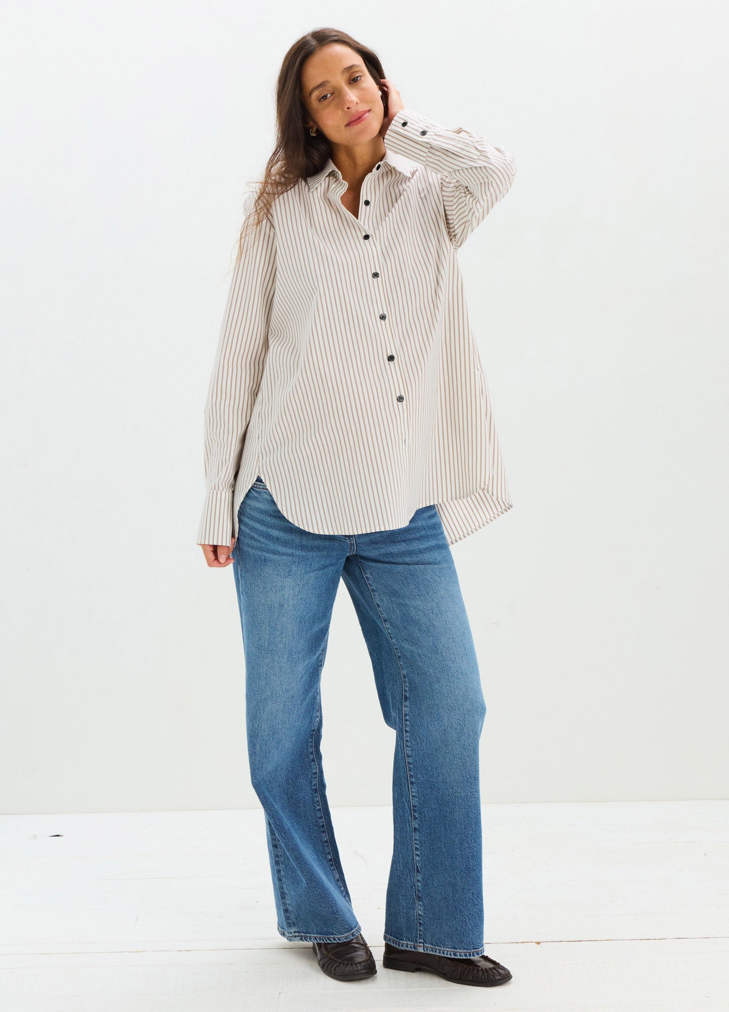 Light beige maternity button-down shirt with black buttons, relaxed fit, paired with blue jeans.