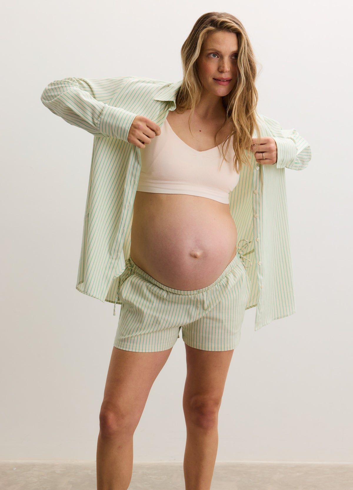 Light green maternity buttondown shirt worn open over matching shorts and a pale pink maternity bralette.