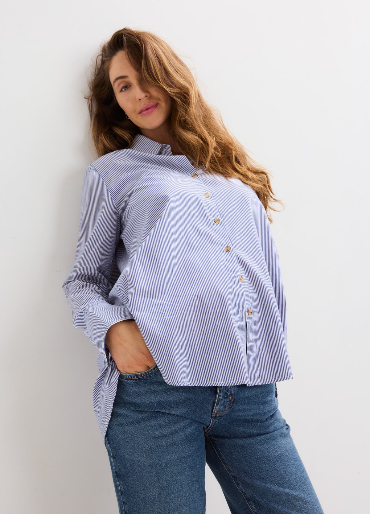 Light blue maternity button-down shirt with a relaxed fit, long sleeves, and a curved hem paired with jeans.