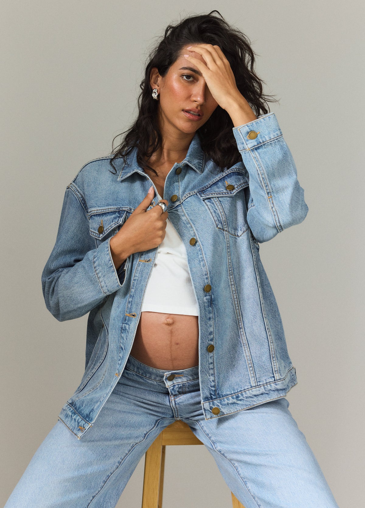 Light wash maternity jean jacket with button front worn open over white top on pregnant model.