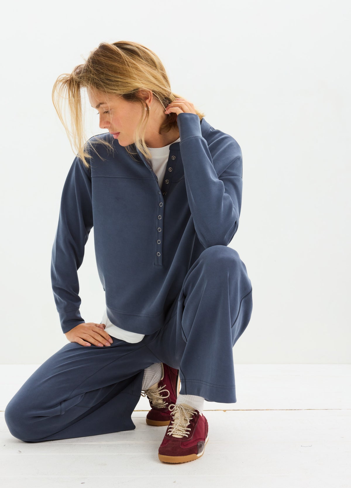 Navy blue maternity pullover with buttoned collar, soft fabric, paired with matching pants and burgundy sneakers.