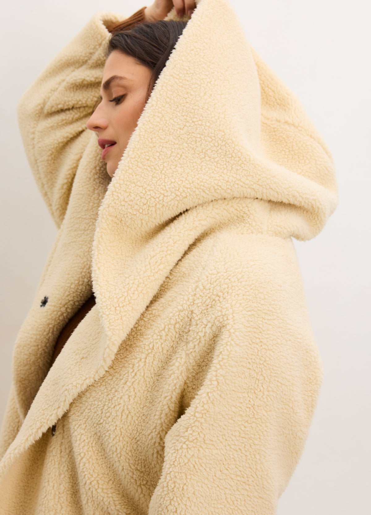 Warm vanilla shearling cocoon coat with oversized hood, styled on pregnant model for maternity wear.