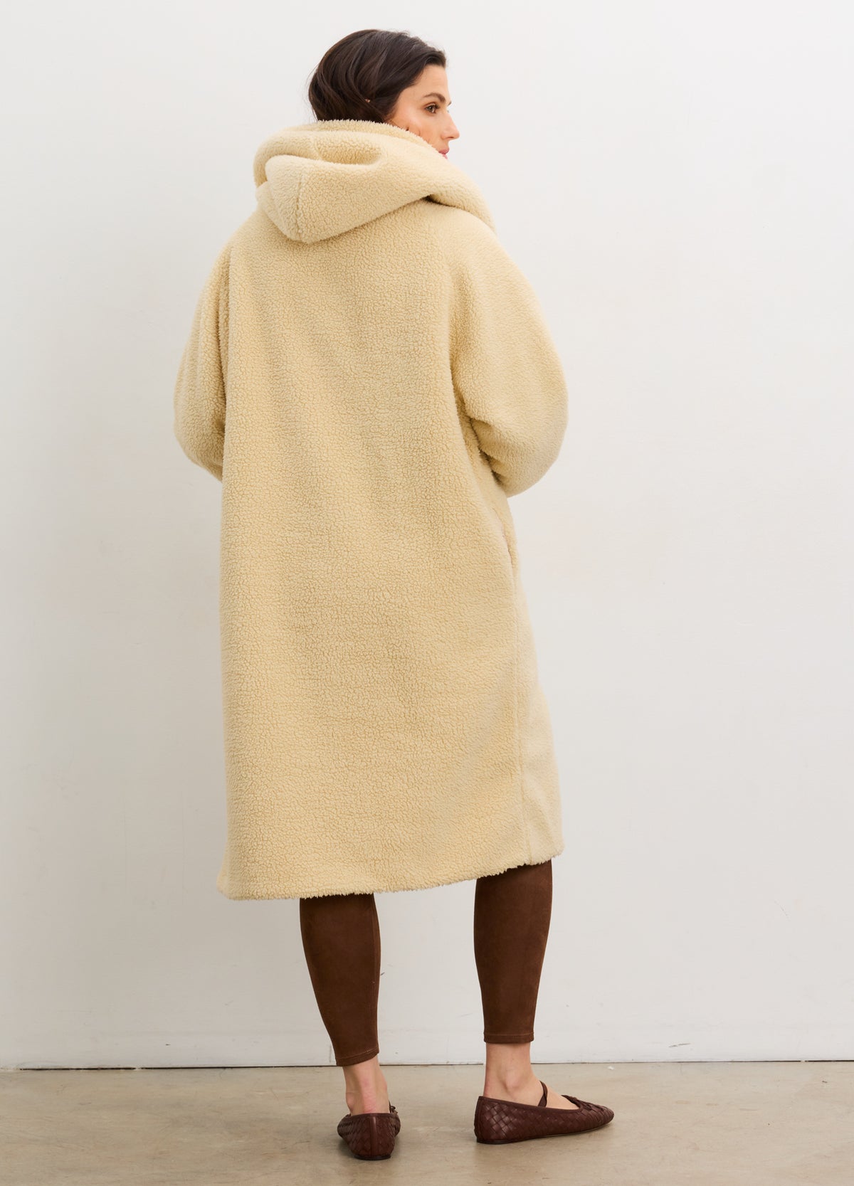 Long cream shearling coat with oversized hood and relaxed cocoon shape, worn over maternity wear.
