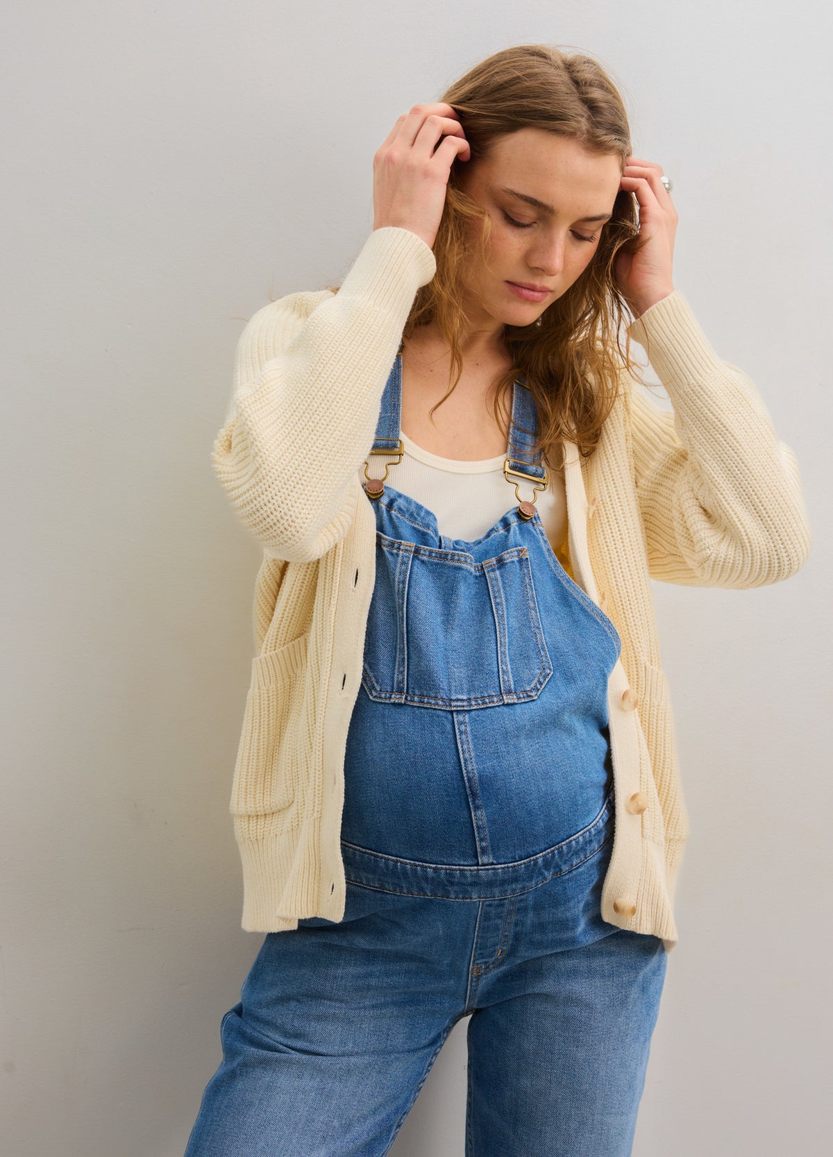 Ivory cotton cardigan with buttons, worn open over a maternity denim overall and white top.