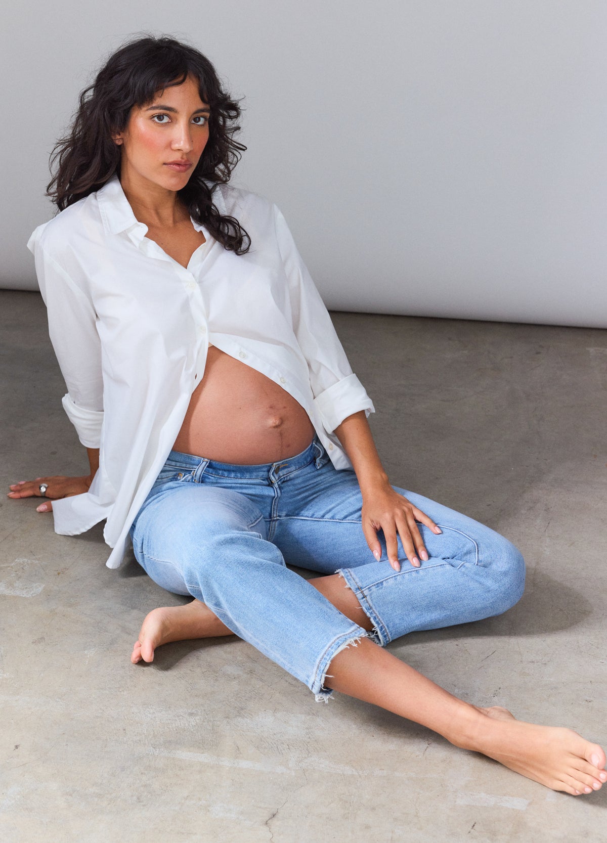 Light blue cropped maternity jeans with stretchy panel over belly, styled with white button-up shirt.