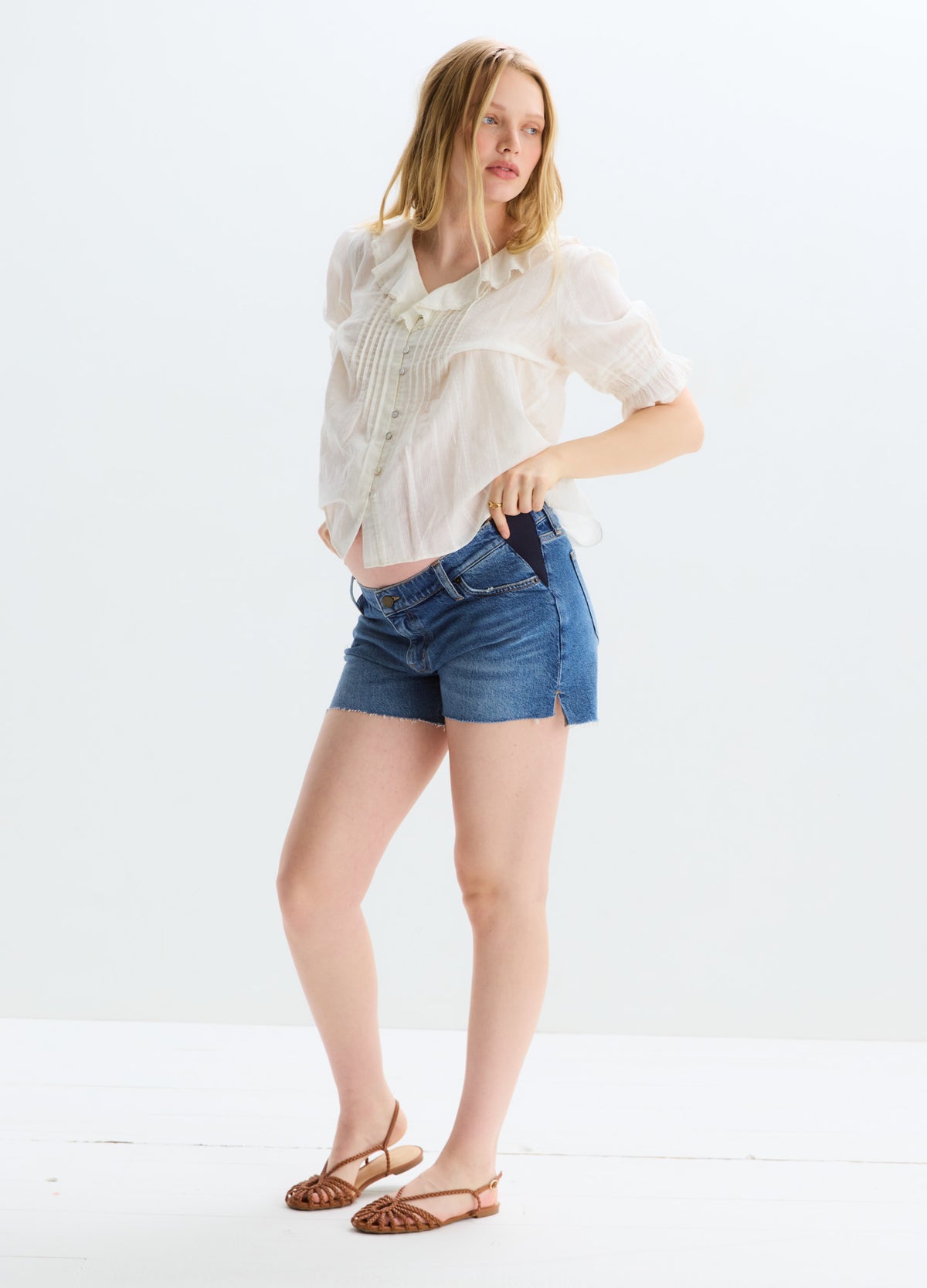Blue denim maternity shorts with cut-off hem and stretchy panel designed for pregnant women.