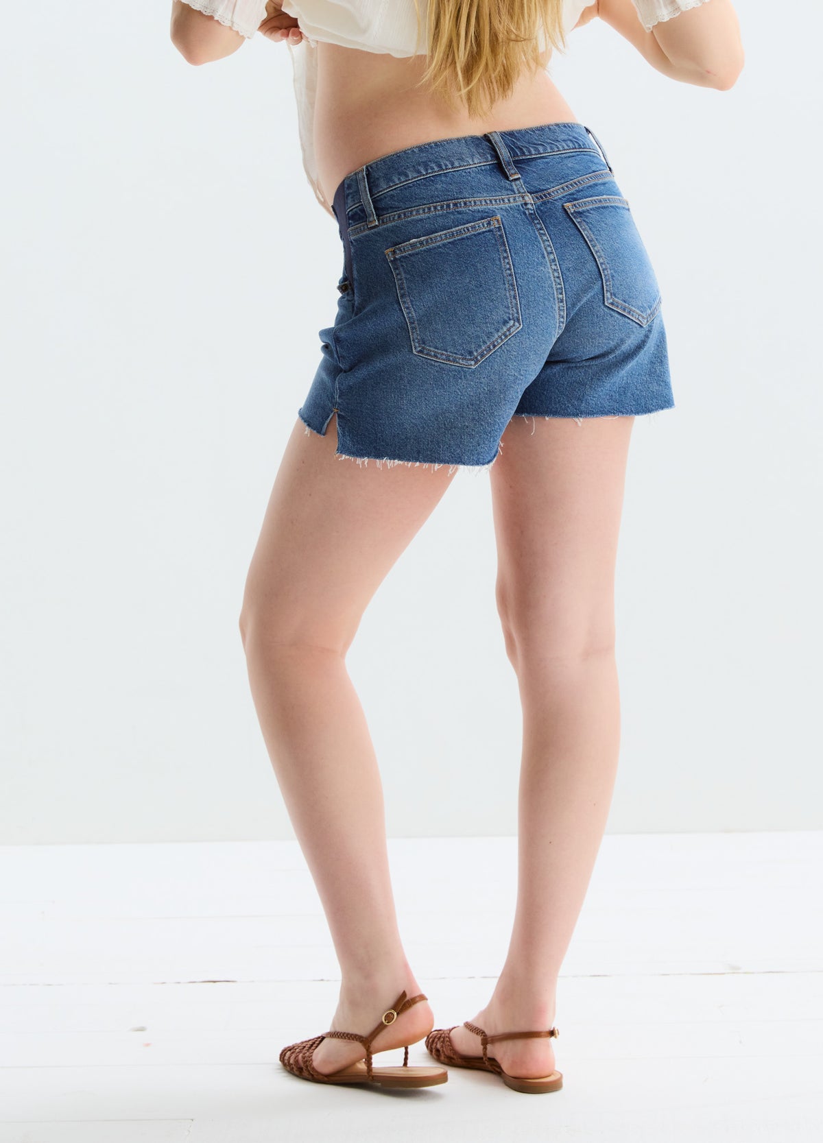 Dark blue denim maternity shorts with a frayed hem and stretchy side panels designed for pregnant women.