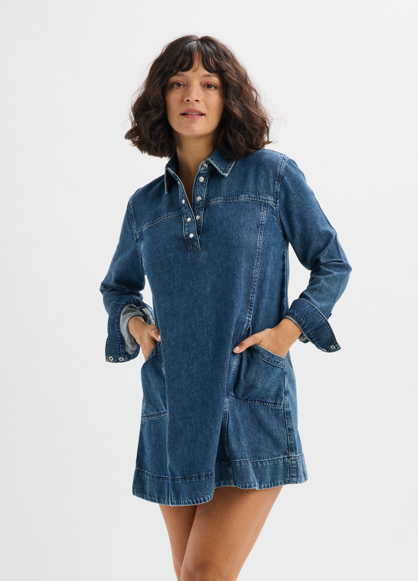 Blue denim mini dress with long sleeves, collar, button placket, front pockets, and loose fit designed for maternity wear.
