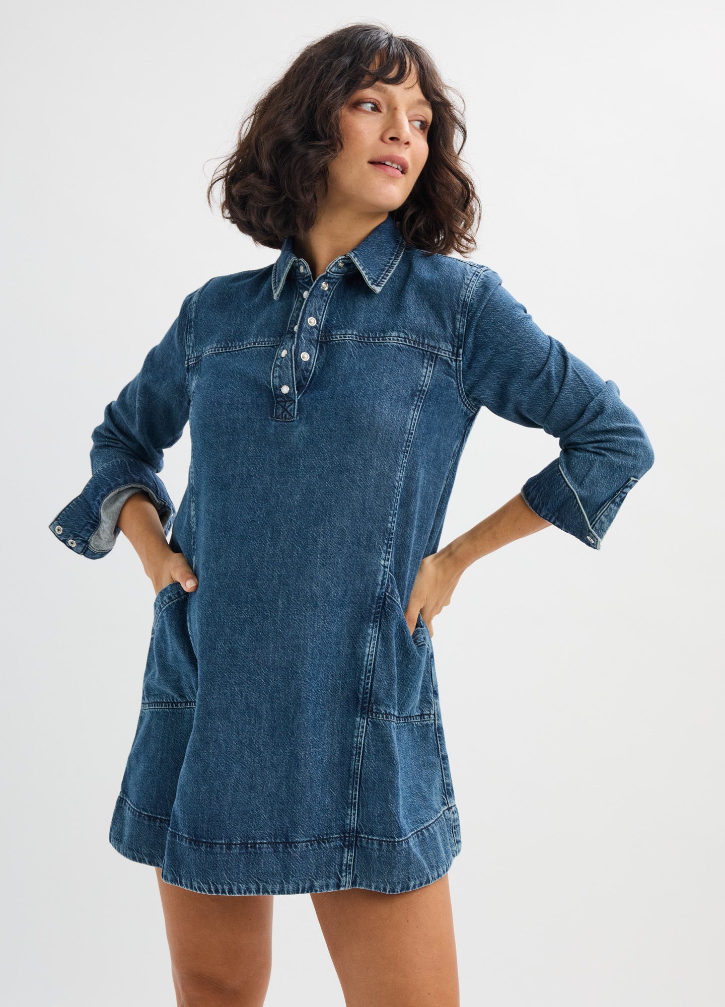 Dark blue denim mini dress with long sleeves, front buttons, collar, and large front pockets, designed for maternity wear.