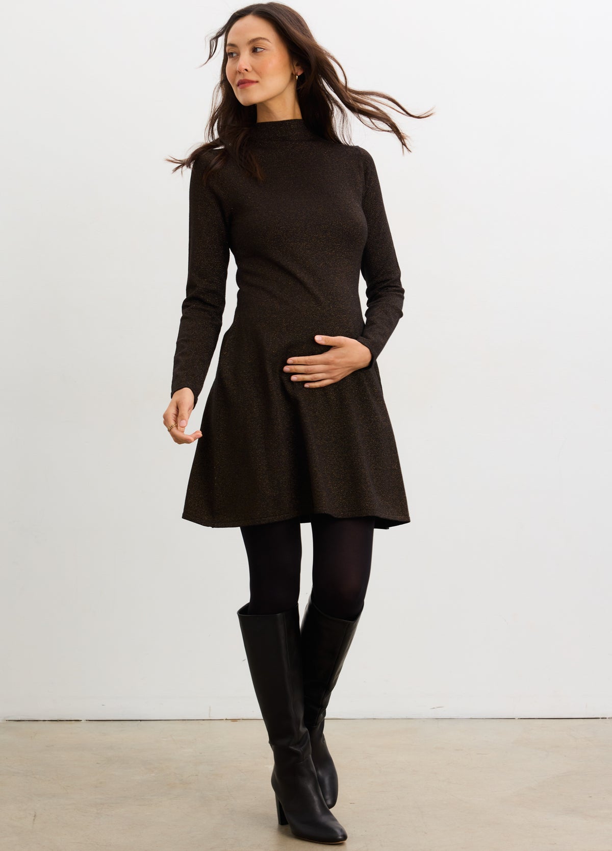 Black long-sleeve maternity knit mini dress with a high neckline and fitted waist, styled with black tights and knee-high.