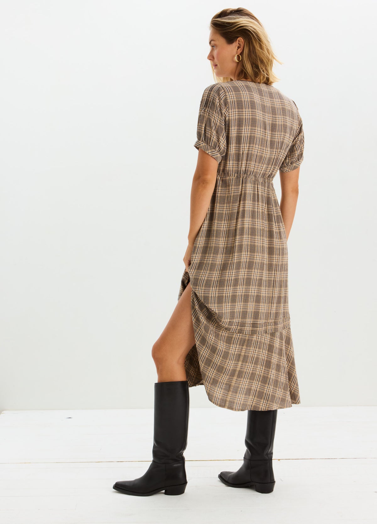 Taupe and brown plaid maternity nursing dress with short puff sleeves and side slit, styled with black knee-high boots.