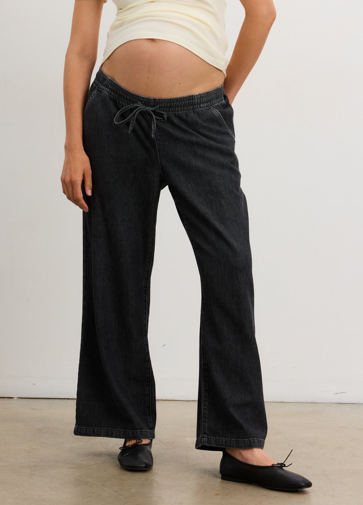 Black wide-leg maternity denim pants with adjustable drawstring waist and soft drapey fabric.