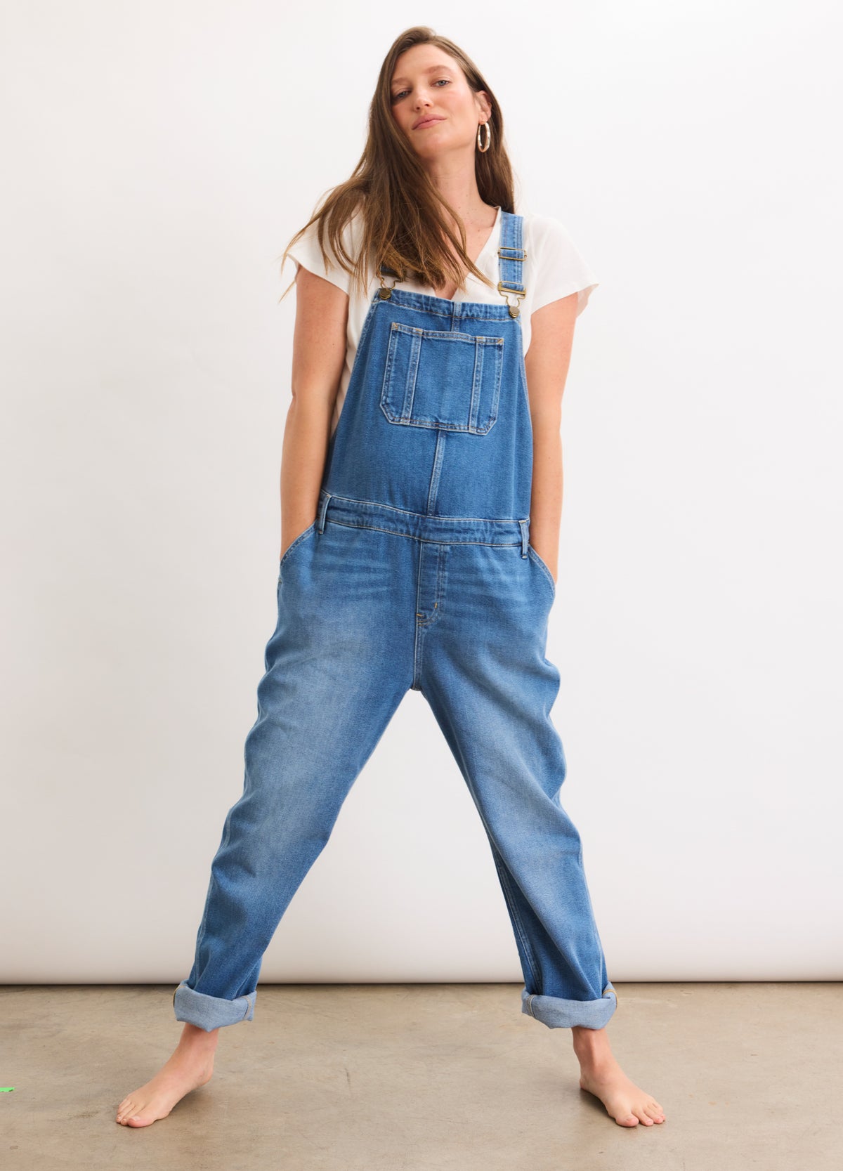 Blue denim maternity overall with adjustable straps and front pocket, worn over white short-sleeve top.