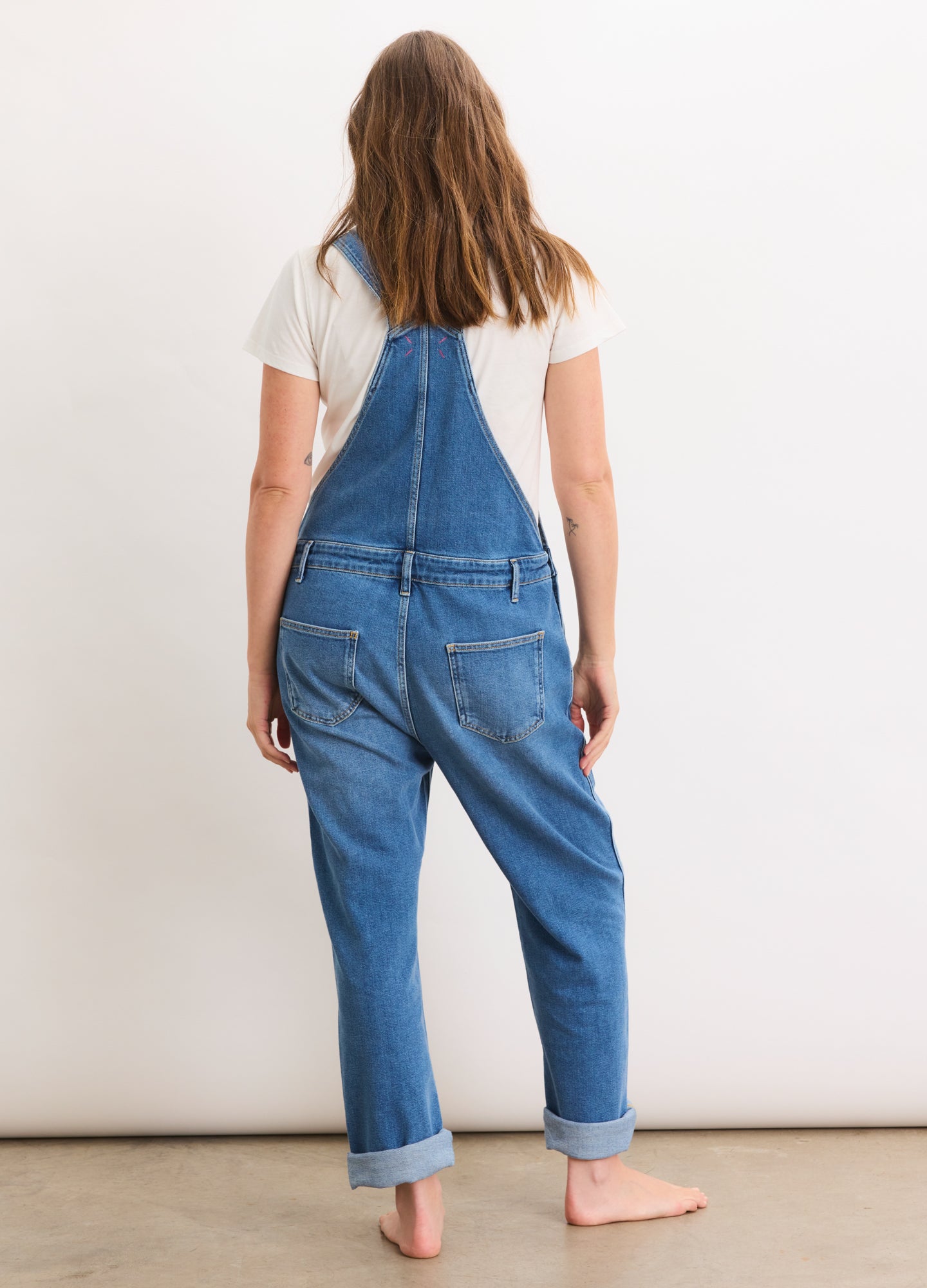 Blue denim maternity overalls with adjustable shoulder straps and rolled cuffs, worn over a white short-sleeve shirt.