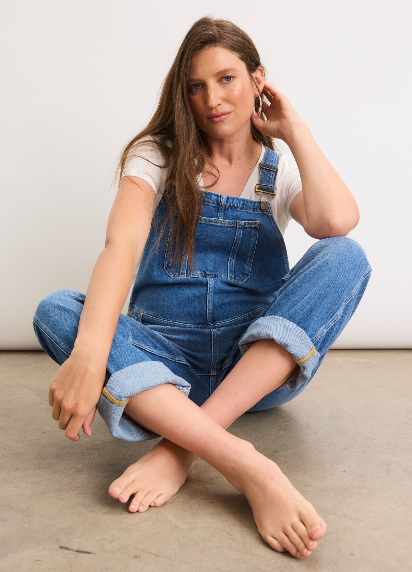 Blue denim maternity overalls with adjustable shoulder straps and rolled cuffs, styled with a white short-sleeve top.