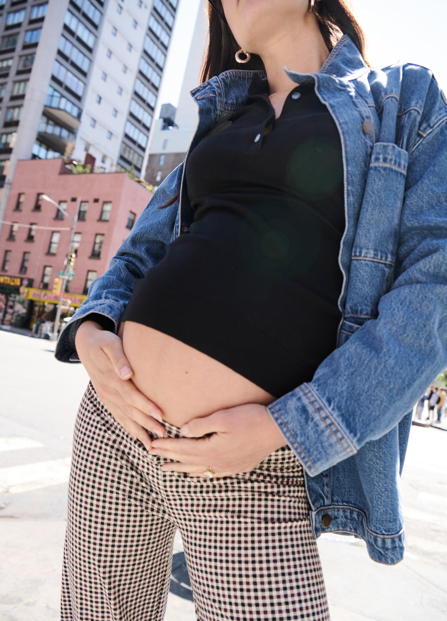 Light blue denim utility jacket layered over a black maternity top, styled with gingham pants, highlighting a pregnant belly.