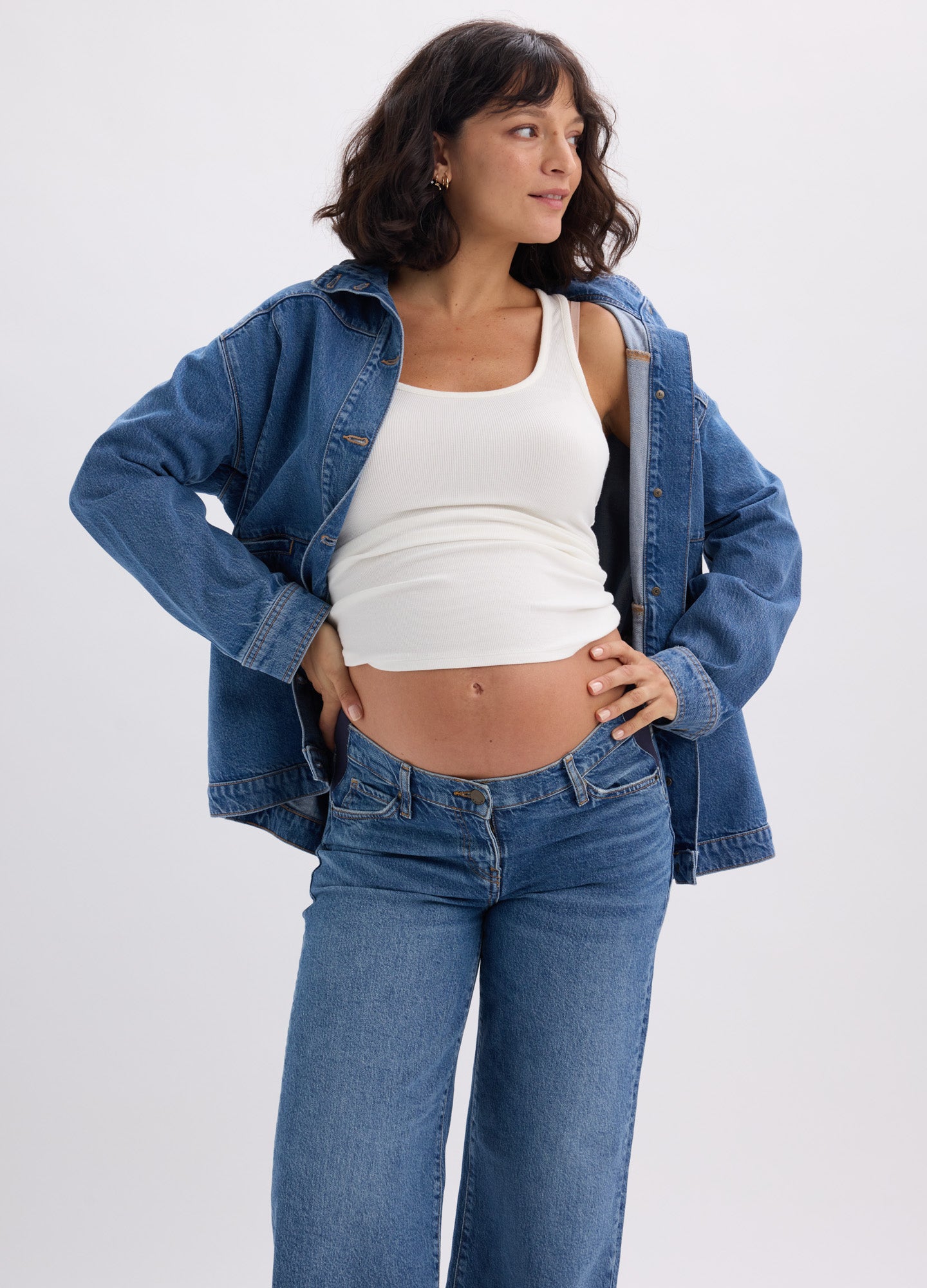 Blue denim utility jacket with button front and chest pockets, styled open over white tank top on pregnant model.