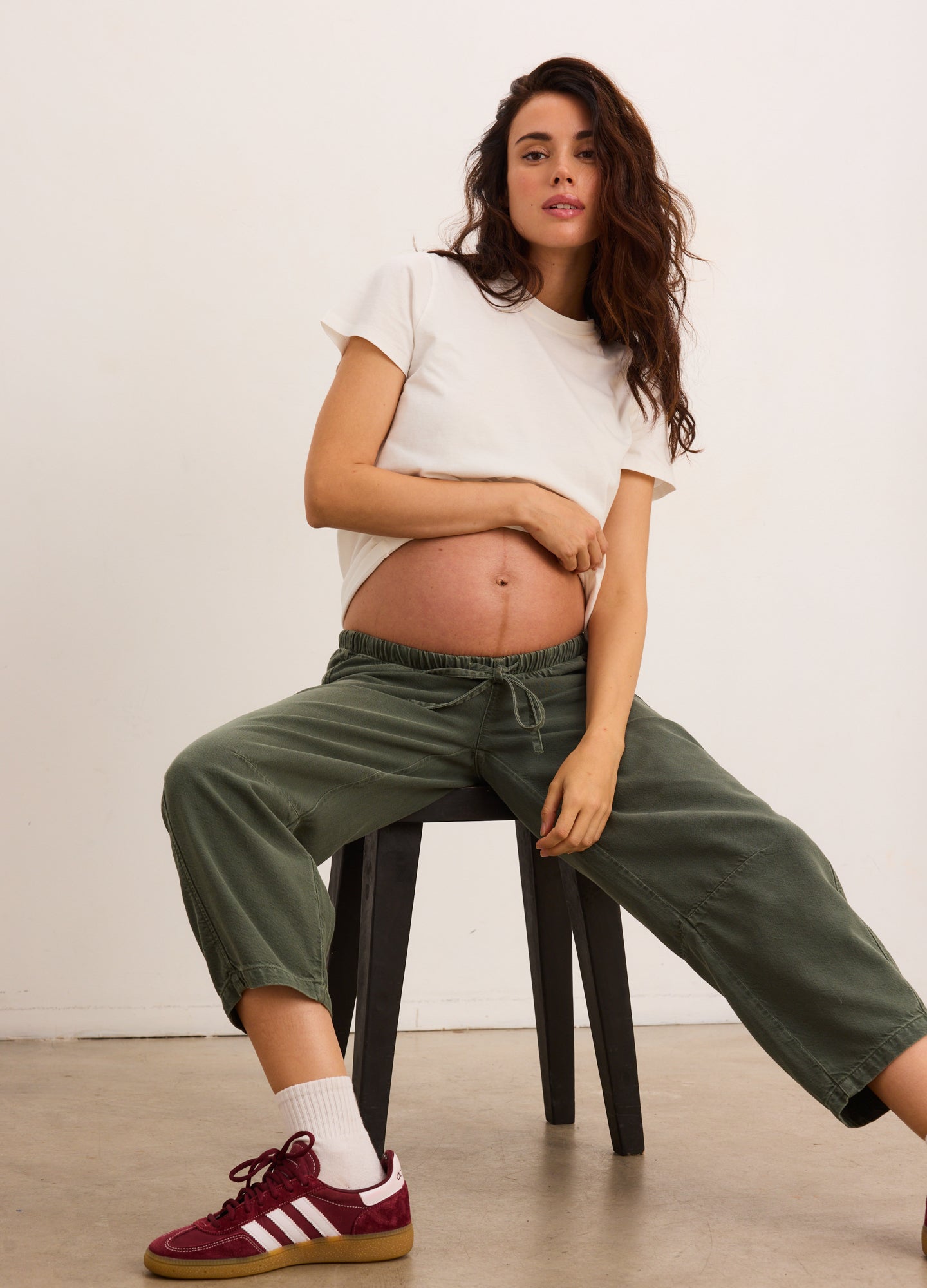 Olive green maternity denim barrel pants with relaxed fit and elastic waistband, worn by pregnant model with cropped white.