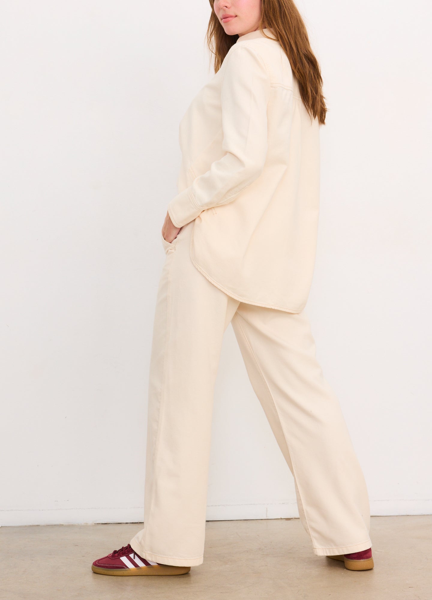 Cream-colored drapey denim boyfriend shirt with long sleeves, worn untucked over matching wide-leg pants.