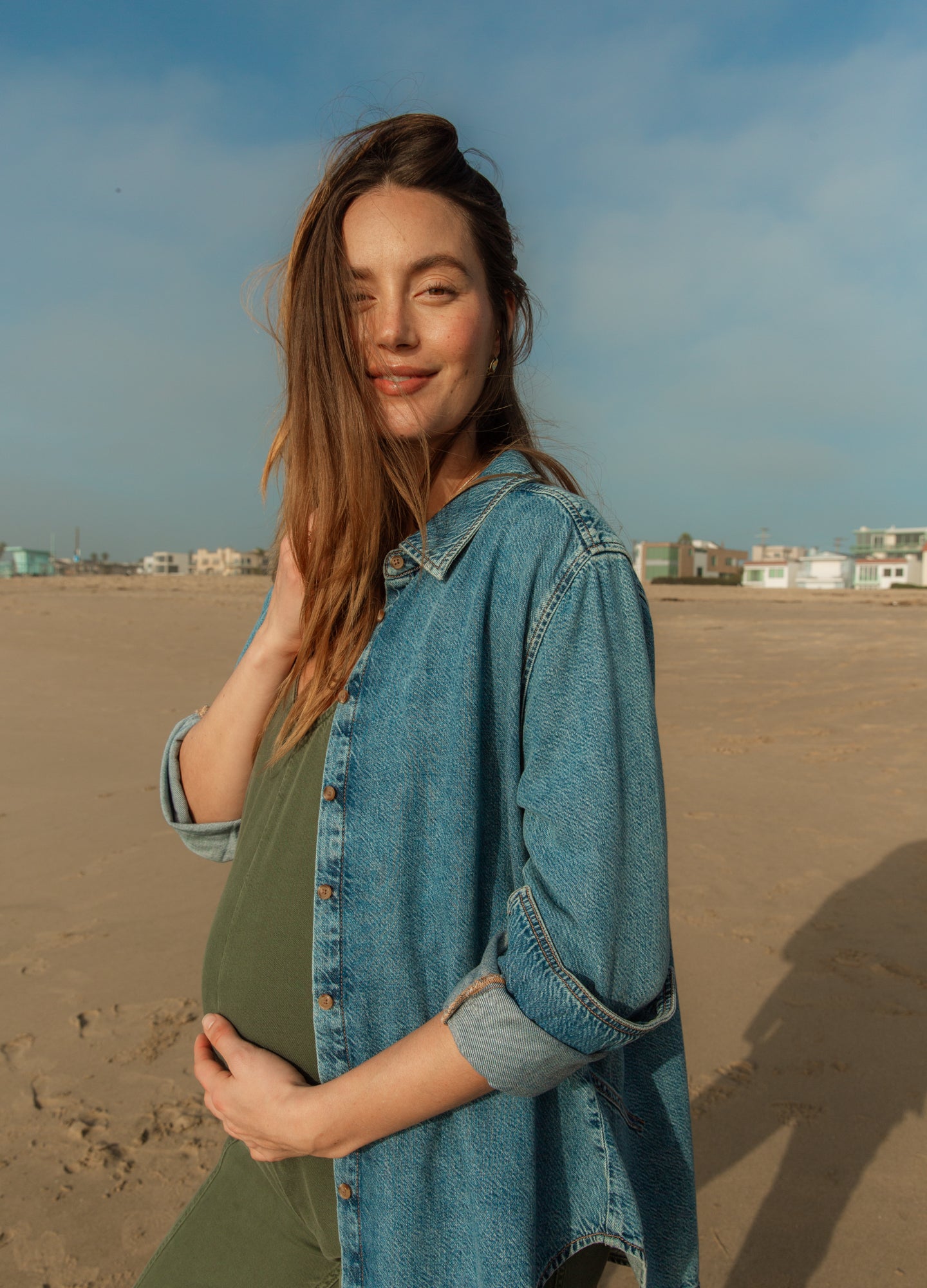 Light blue denim boyfriend shirt worn open over olive green maternity tank top on pregnant woman outdoors.