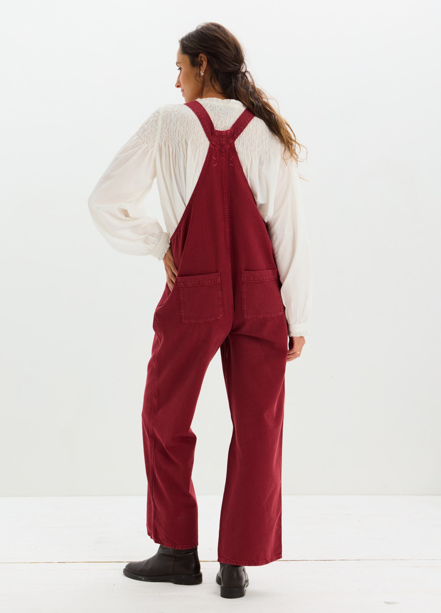 Maternity drapey denim overalls in deep red with wide legs and adjustable shoulder straps worn over a white long-sleeve top.