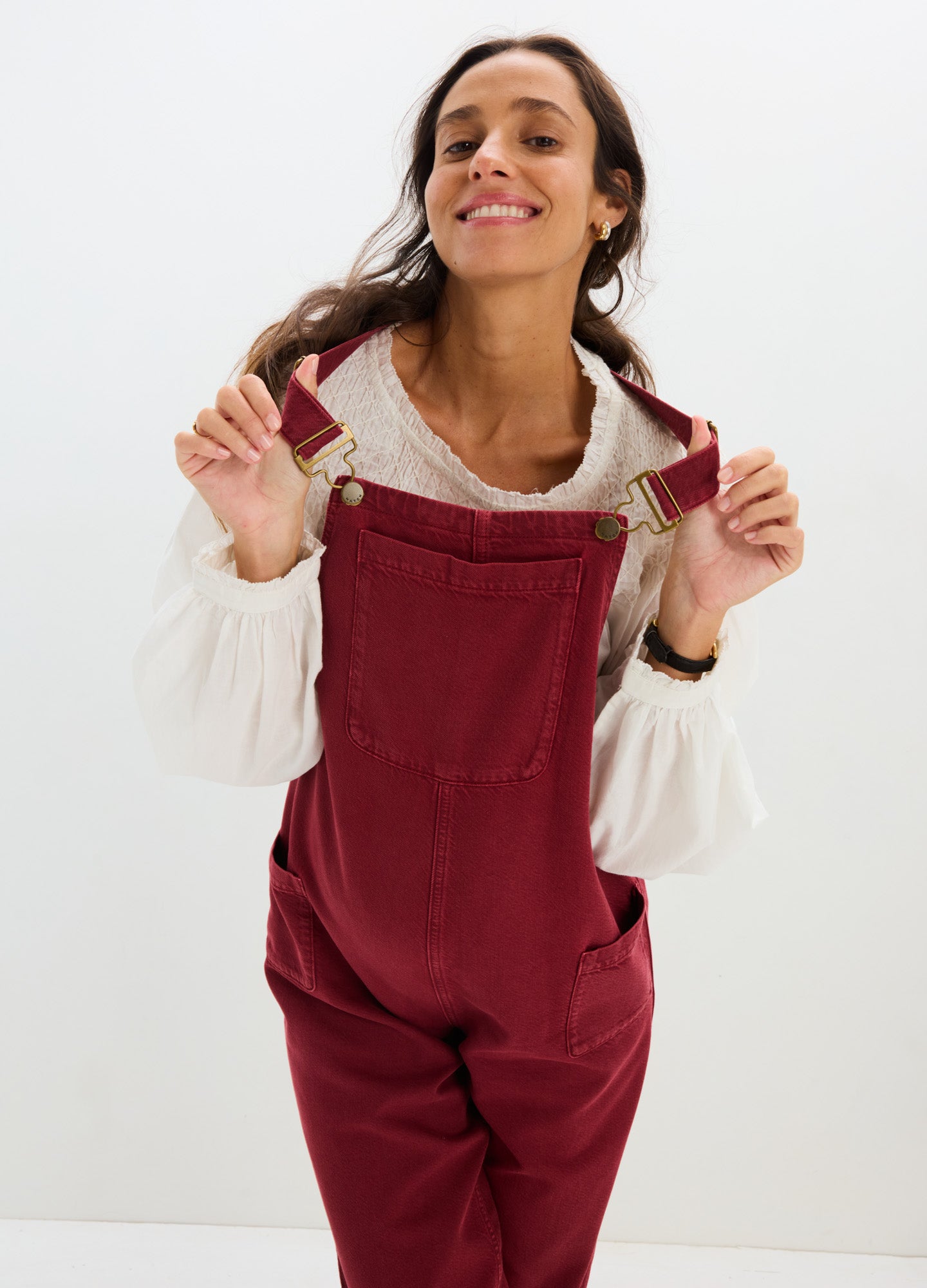 Burgundy maternity denim overalls with adjustable straps and roomy fit, worn with white puff-sleeve blouse.