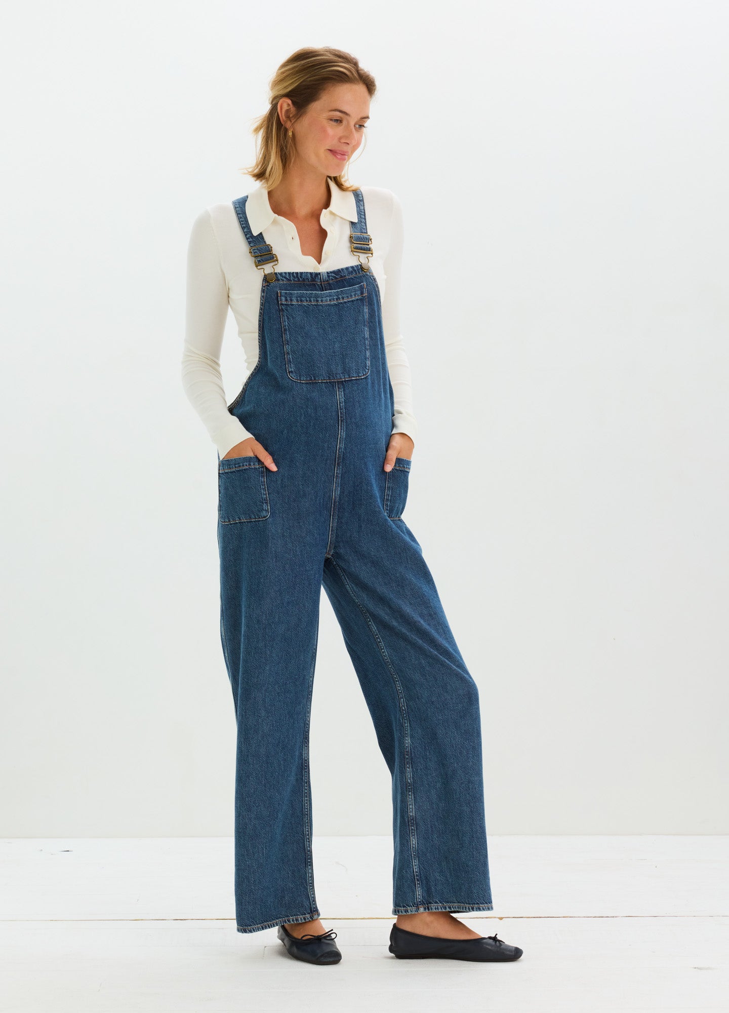 Dark blue denim maternity overall with adjustable straps and front bib pocket, worn with long-sleeve white shirt.