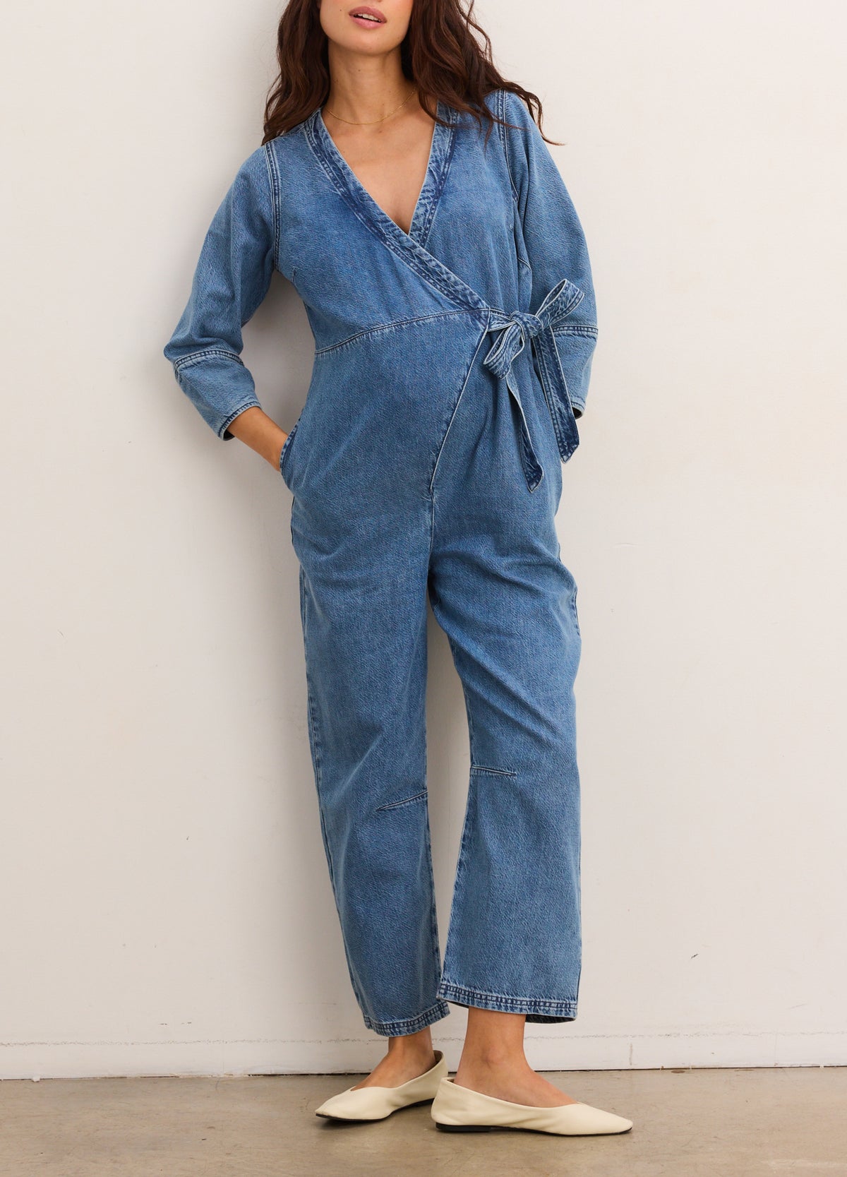 Light blue denim maternity jumpsuit with long sleeves, wrap-front, and tie waist detail.