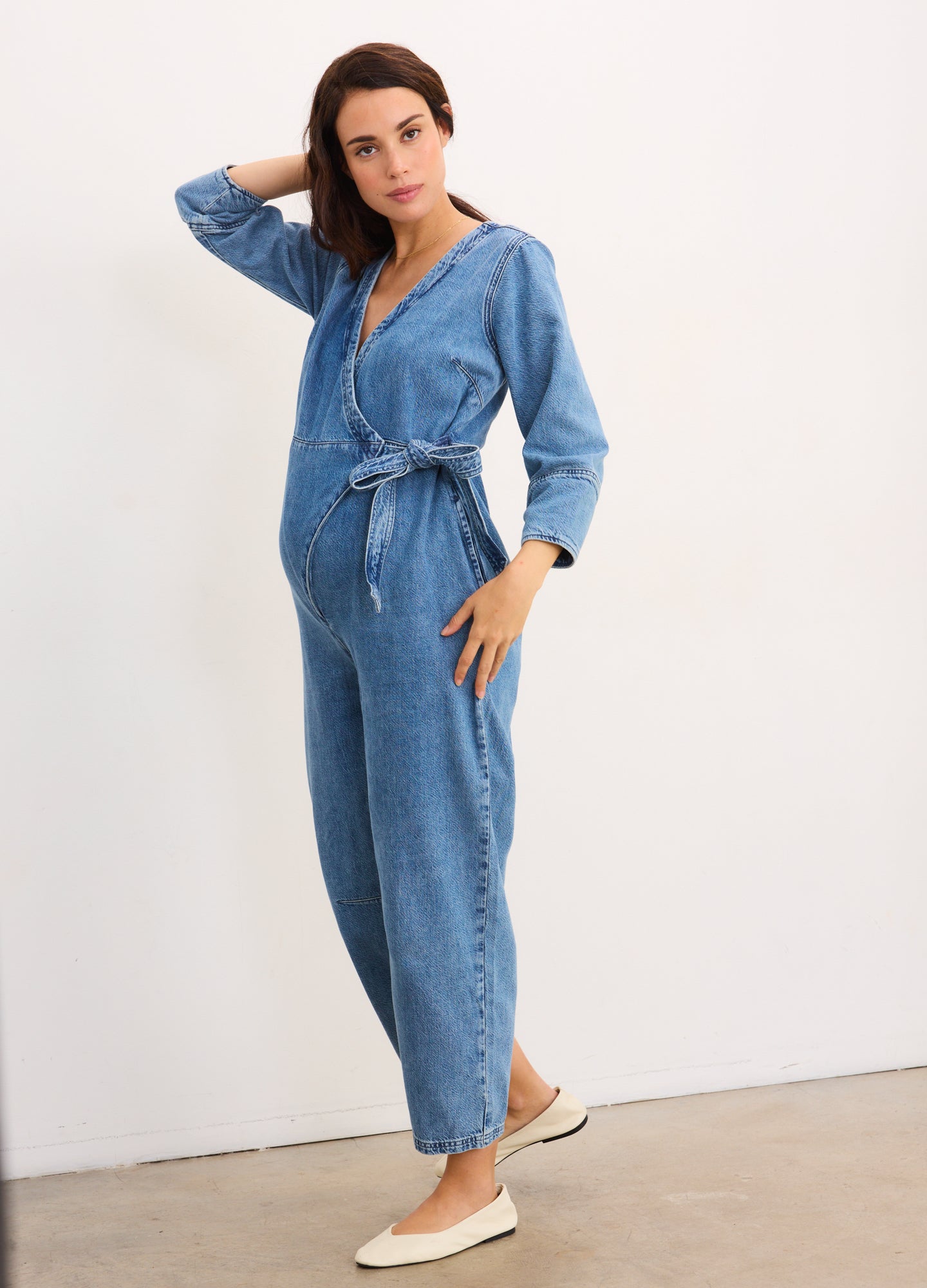 Light blue denim maternity jumpsuit with long sleeves, wrap front, and tie waist belt.