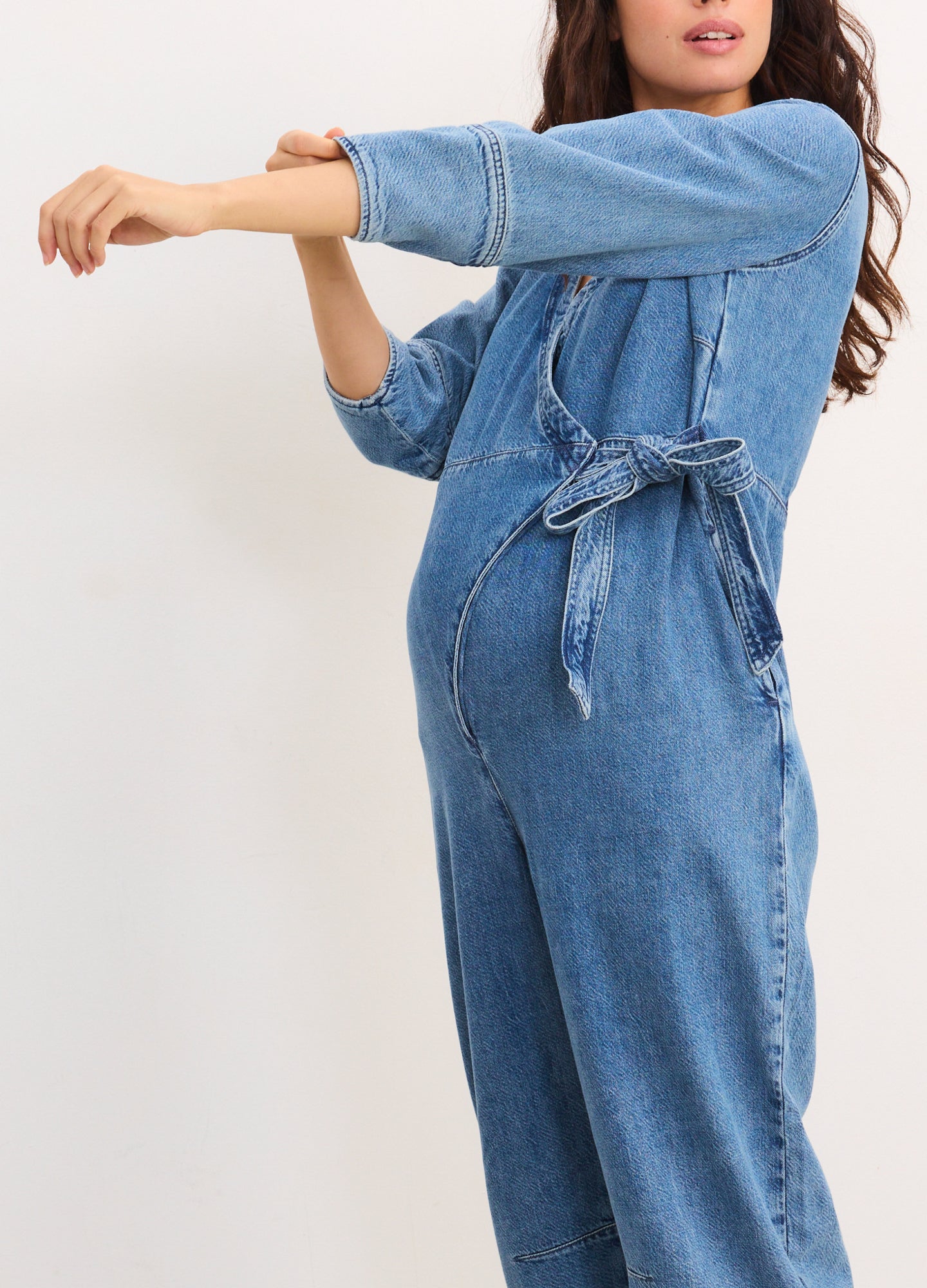 Light blue denim maternity jumpsuit with long sleeves, loose fit, and a self-tie waist belt.