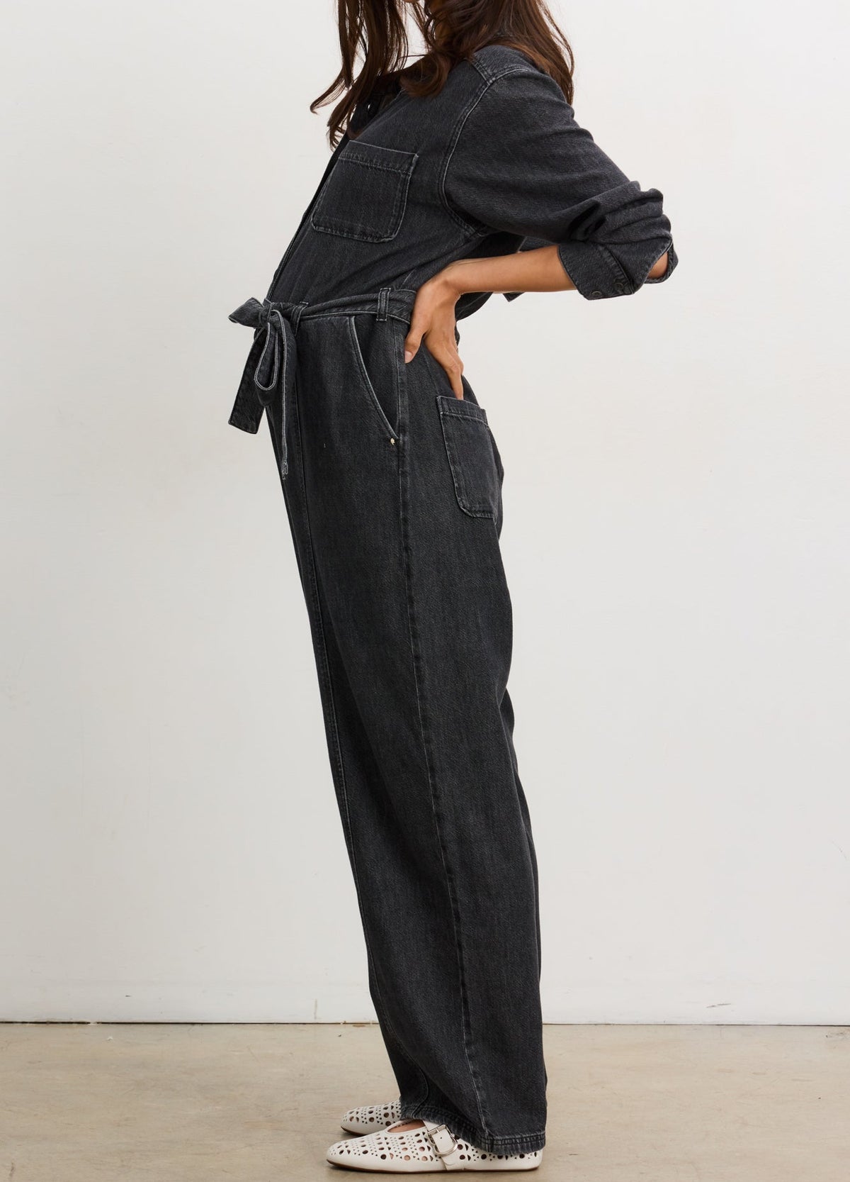 Washed black maternity denim jumpsuit with adjustable waist tie and rolled sleeves on pregnant model.