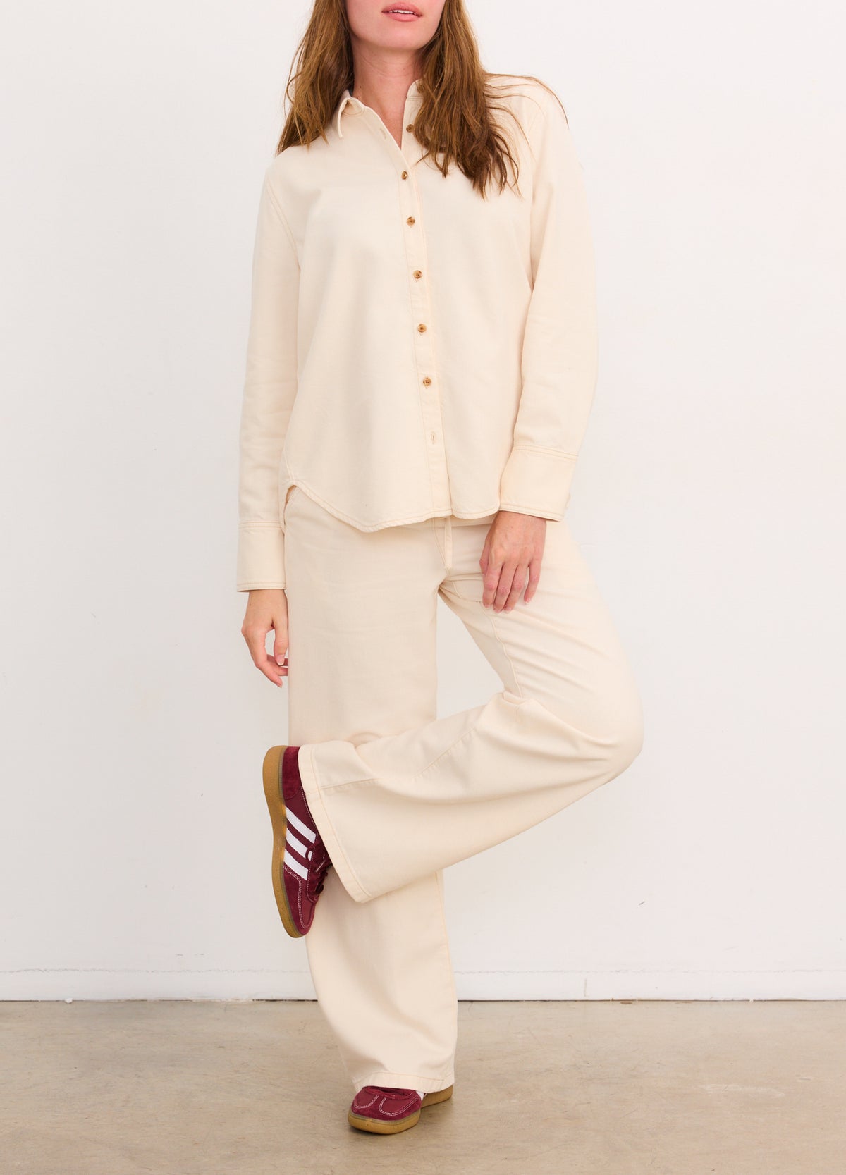 Cream-colored drapey wide-leg maternity denim pants paired with matching button-up shirt and burgundy sneakers.