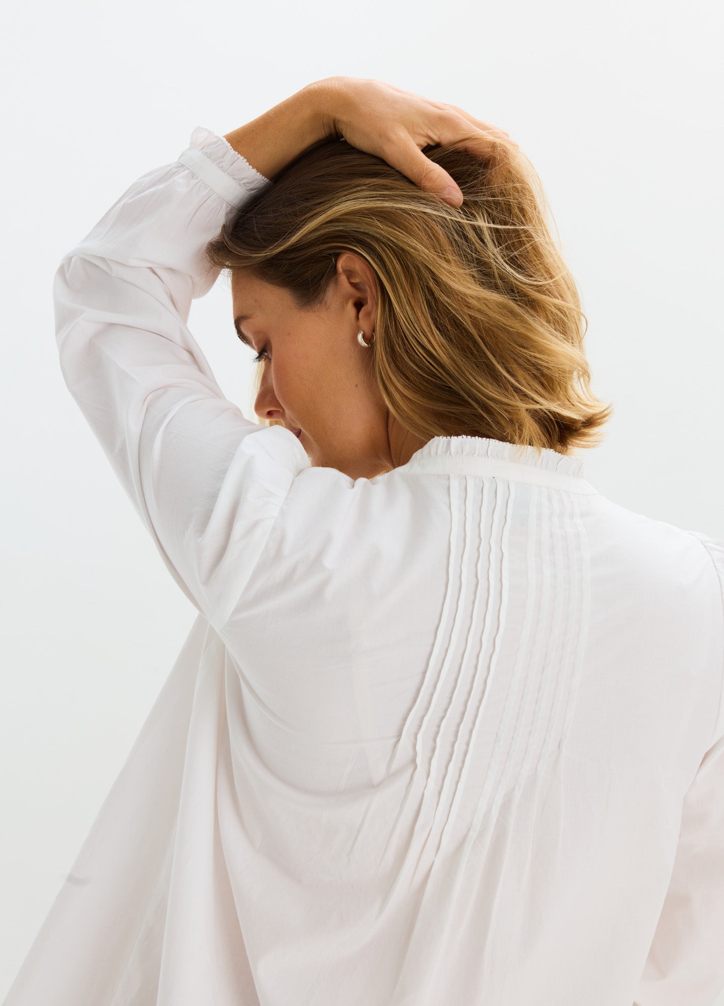White maternity nursing blouse with long sleeves and vertical pintuck details on the back.