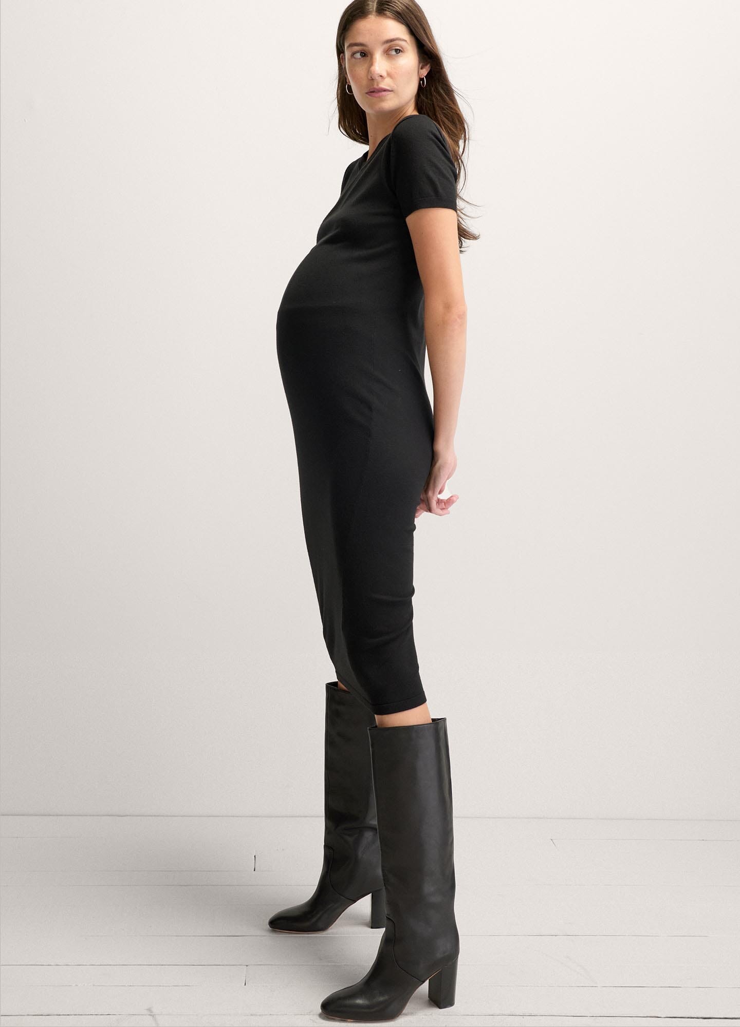 Black fitted knit maternity dress with short sleeves and midi length, styled with black knee-high boots.