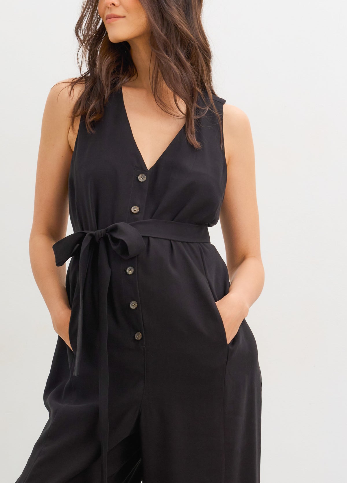The Elliot Jumpsuit - Black sleeveless maternity jumpsuit with V-neck, nursing-friendly buttons, and a tie waist designed for pregnancy and.