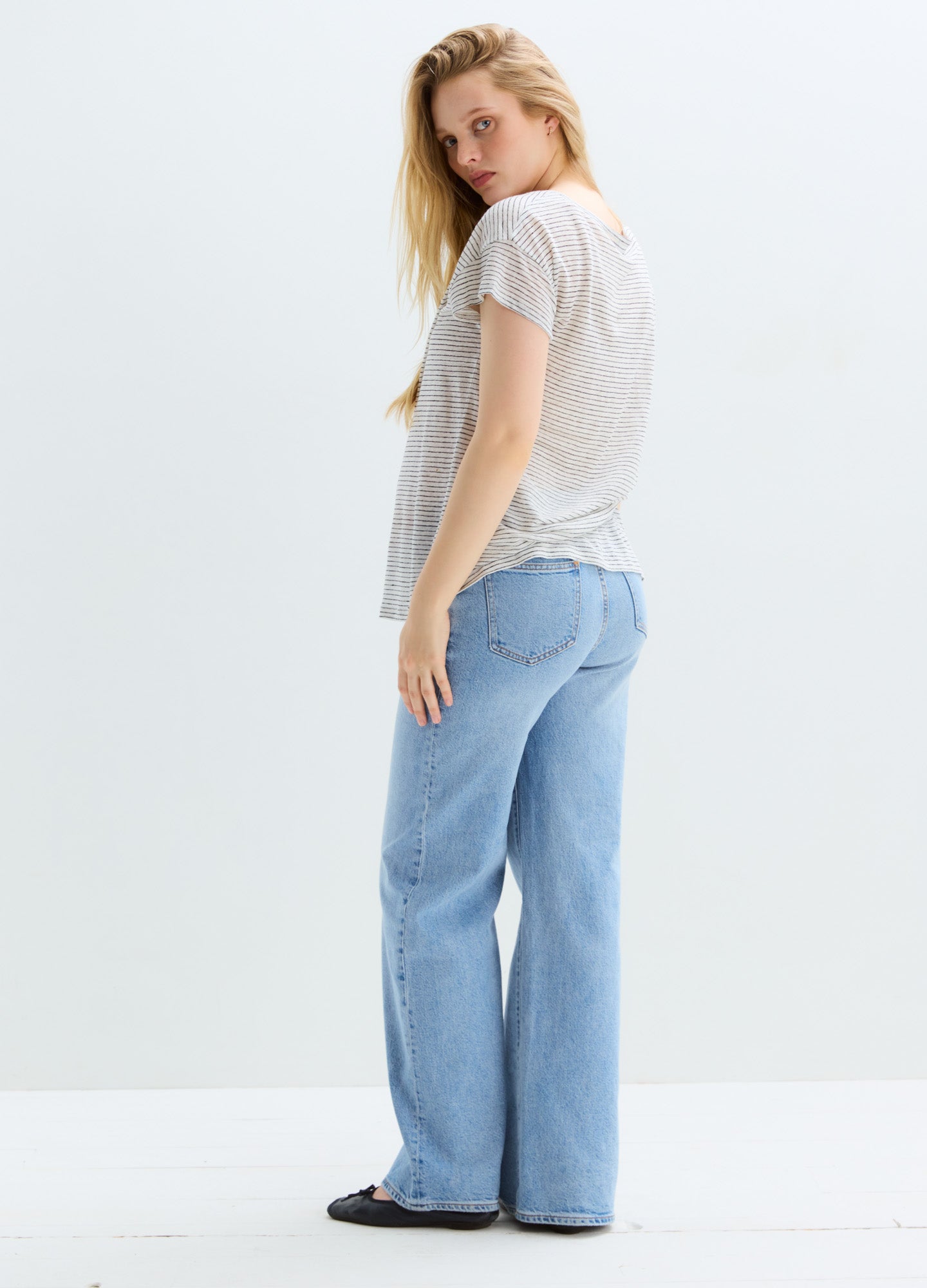 Light blue relaxed wide-leg maternity jeans styled with a casual white blouse and black flats.
